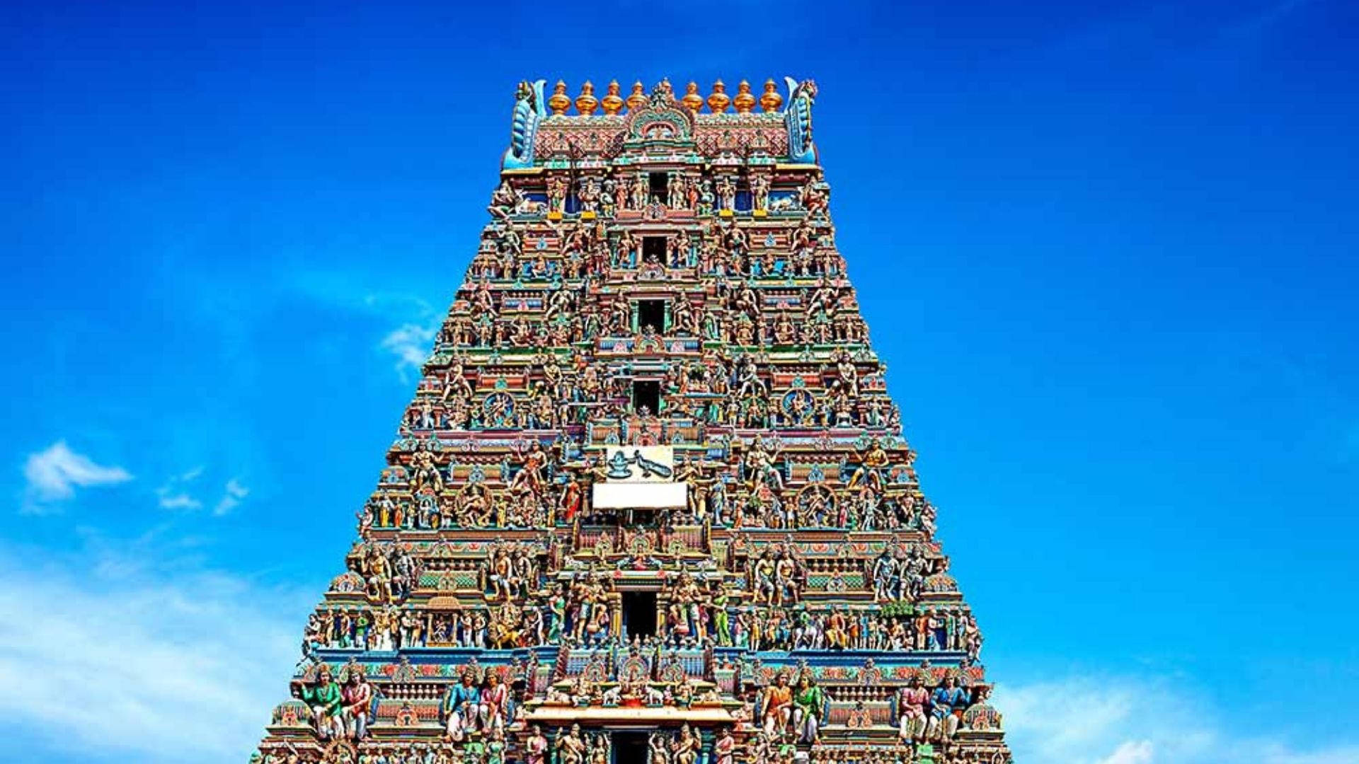 Chennai 桌布 壁紙 — 一座高聳、雕刻精美的印度教寺廟 gopuram 在蔚藍的天空和散落的白色雲朵中升起。
