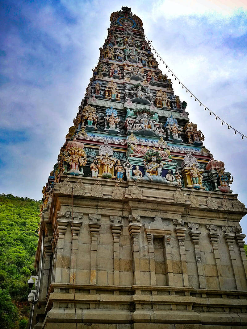 Hindu Temple 桌布 壁紙 — 一座高聳、雕刻精美的印度教寺廟，擁有鮮豔的雕像和色彩繽紛的細節，聳立在部分多雲的天空下。