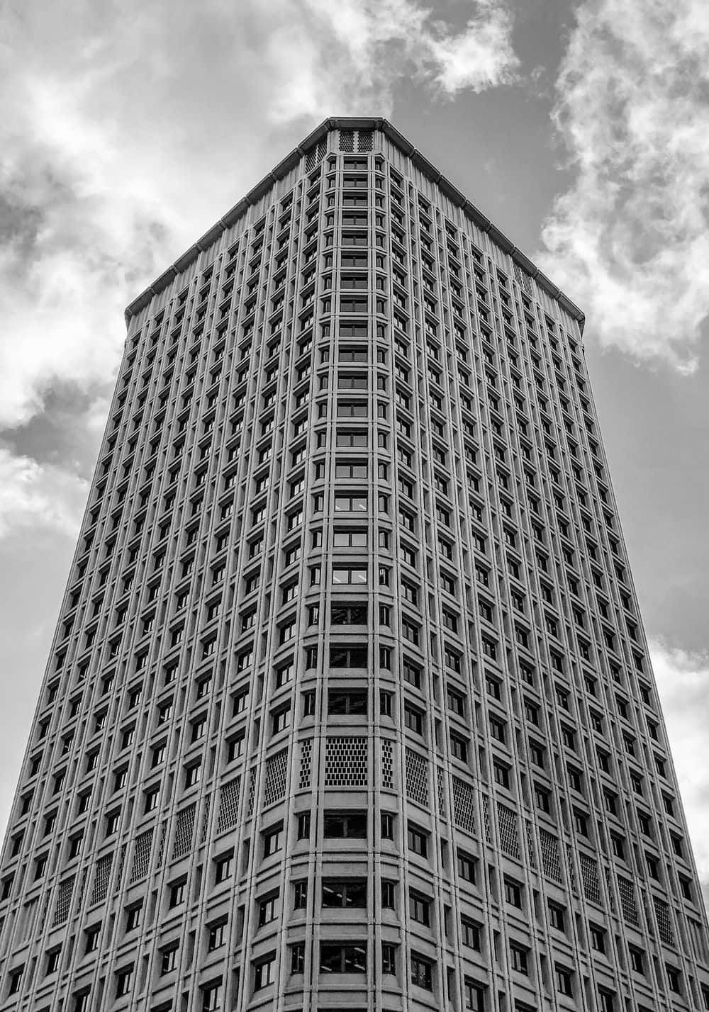 Buildings 桌布 壁紙 — 一座高聳入雲的摩天大樓在戲劇性的低角度黑白拍攝中，聳立於多雲的天空下。