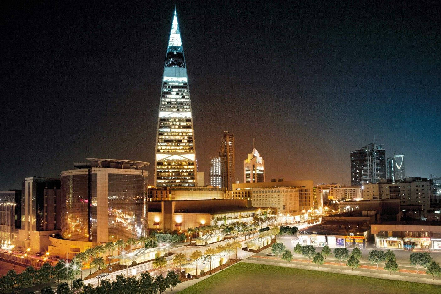 Riyadh 桌布 壁紙 — 一座高聳入雲的發光摩天大樓主宰著充滿活力的城市夜景，下方是閃爍的窗戶和棕櫚樹成蔭的街道。