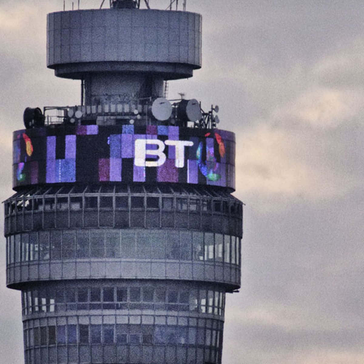 tower 桌布 壁紙 — 一座高聳的BT建築在陰沉的灰色天空中展示了一個充滿活力的數位彩虹標誌。