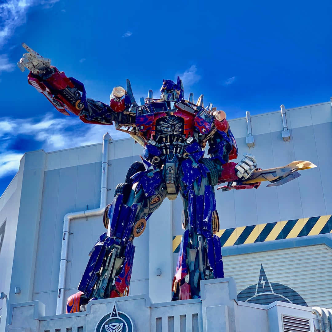 變形金剛 桌布 壁紙 — 一座高聳的Optimus Prime雕像，在藍天白雲下英勇地矗立。