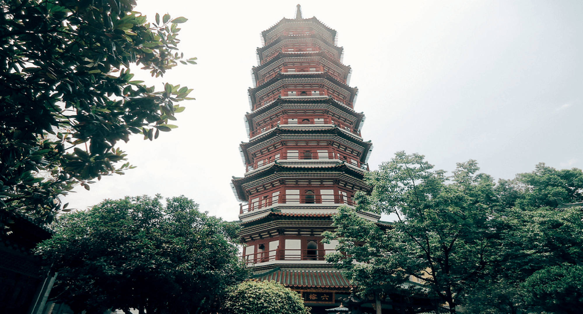Guangzhou 桌布 壁紙 — 一座高聳的傳統中式寶塔在陰天中從茂密的綠樹中升起。