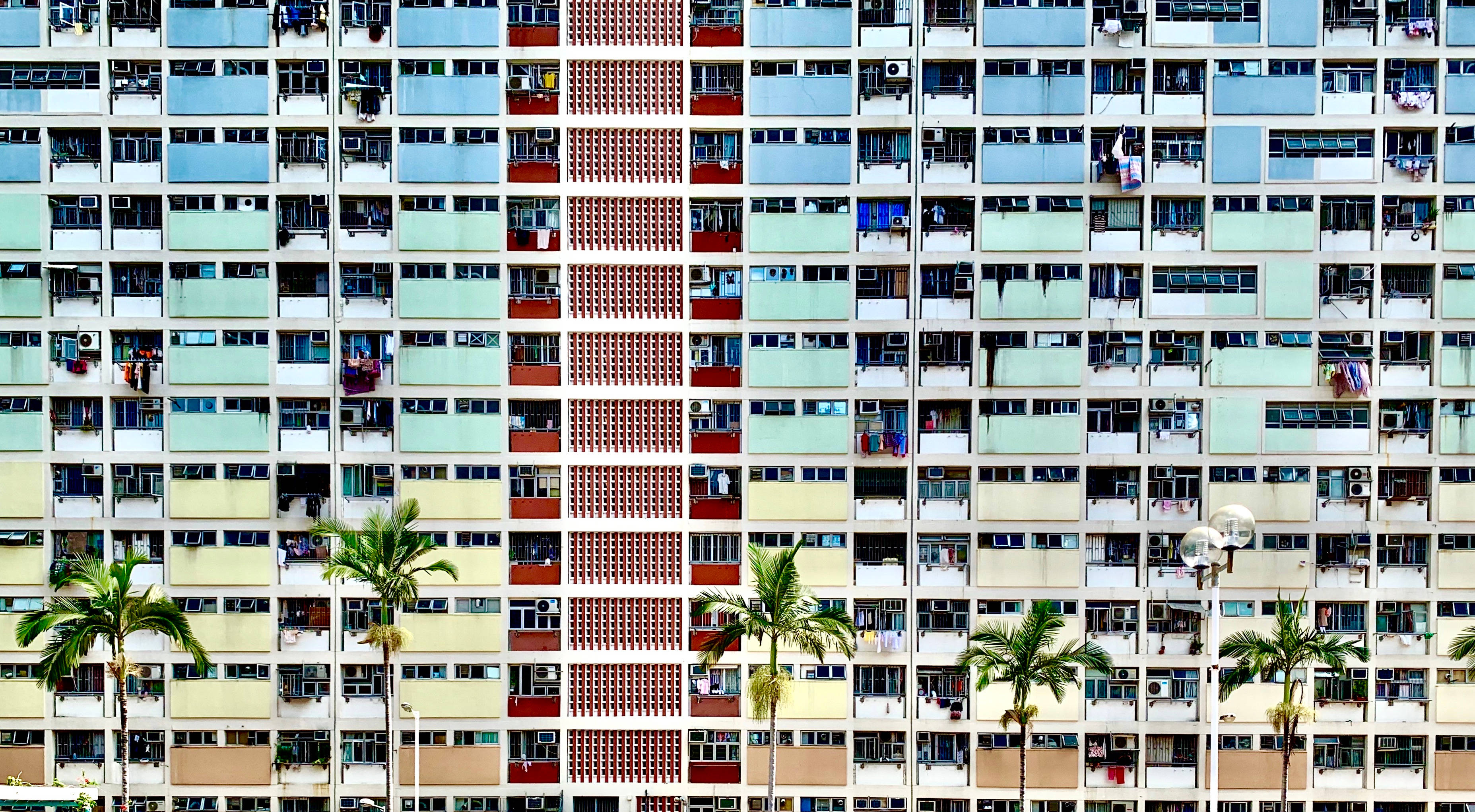 Hong Kong 桌布 壁紙 — 一座高聳的公寓大樓，下方有色彩繽紛的陽台和棕櫚樹，在明亮的日光下。