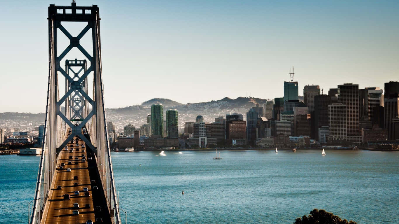 1366x768 San Francisco 桌布 壁紙 — 一座高聳的吊橋橫跨碧綠色的海水，在晴朗的藍天下延伸向密集的城市天際線。