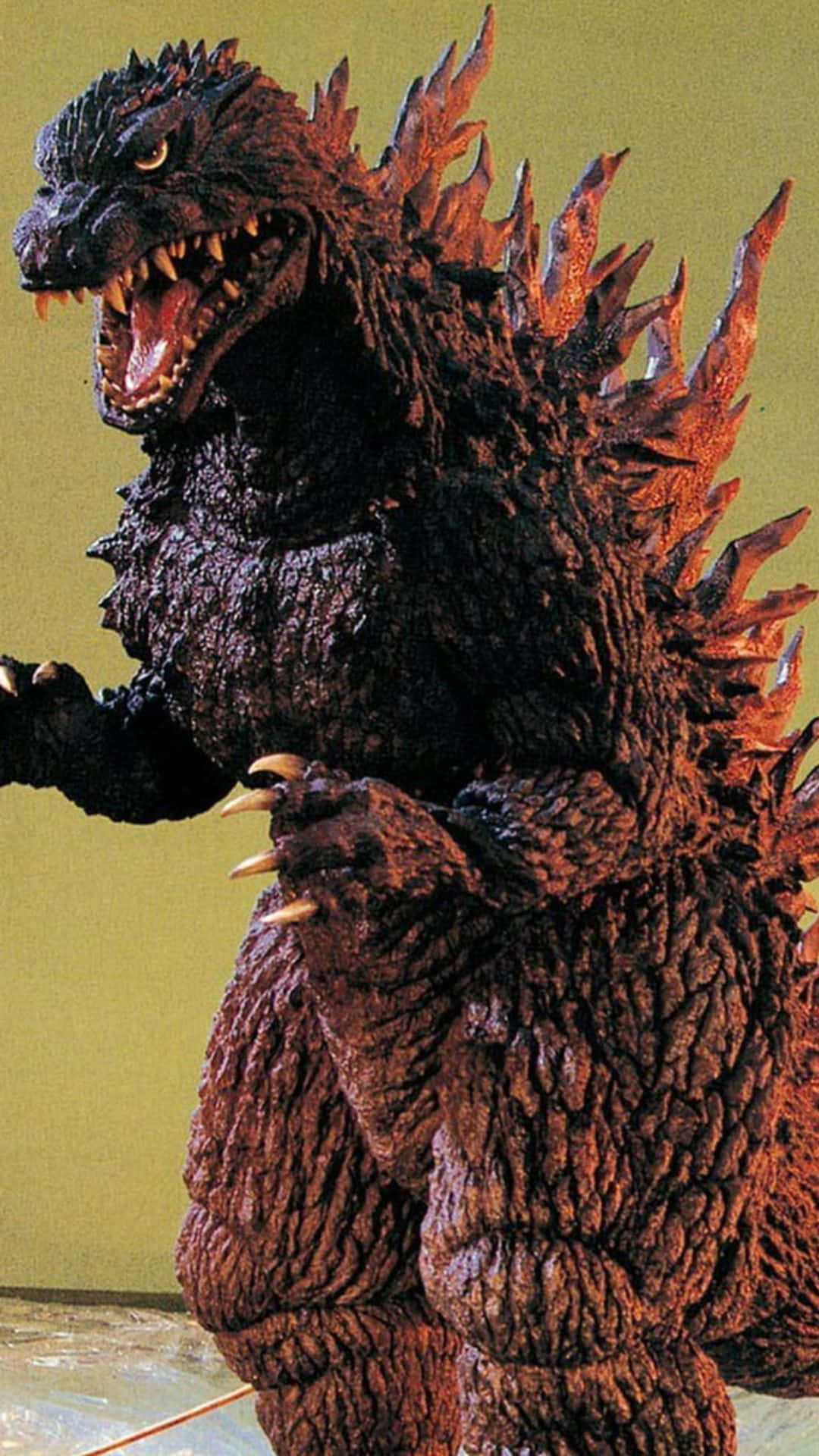 Godzilla 2000 桌布 壁紙 — 一座高聳的哥吉拉雕像，帶有紋理的深色鱗片和發光的眼睛，在純黃色牆壁前威嚴地站立。