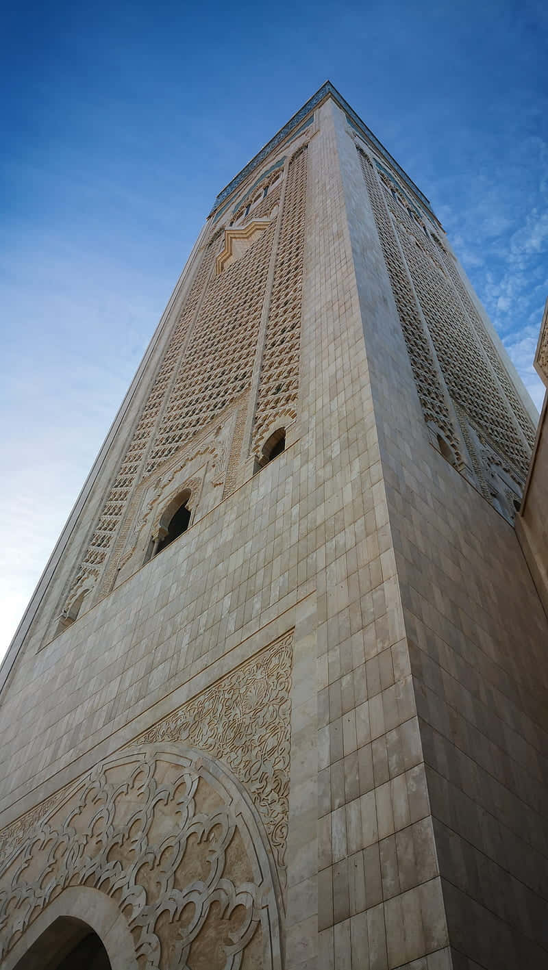Mosque 桌布 壁紙 — 一座高聳的宣禮塔，帶有複雜的幾何雕刻，在明亮的日光下襯著清澈的藍天聳立。