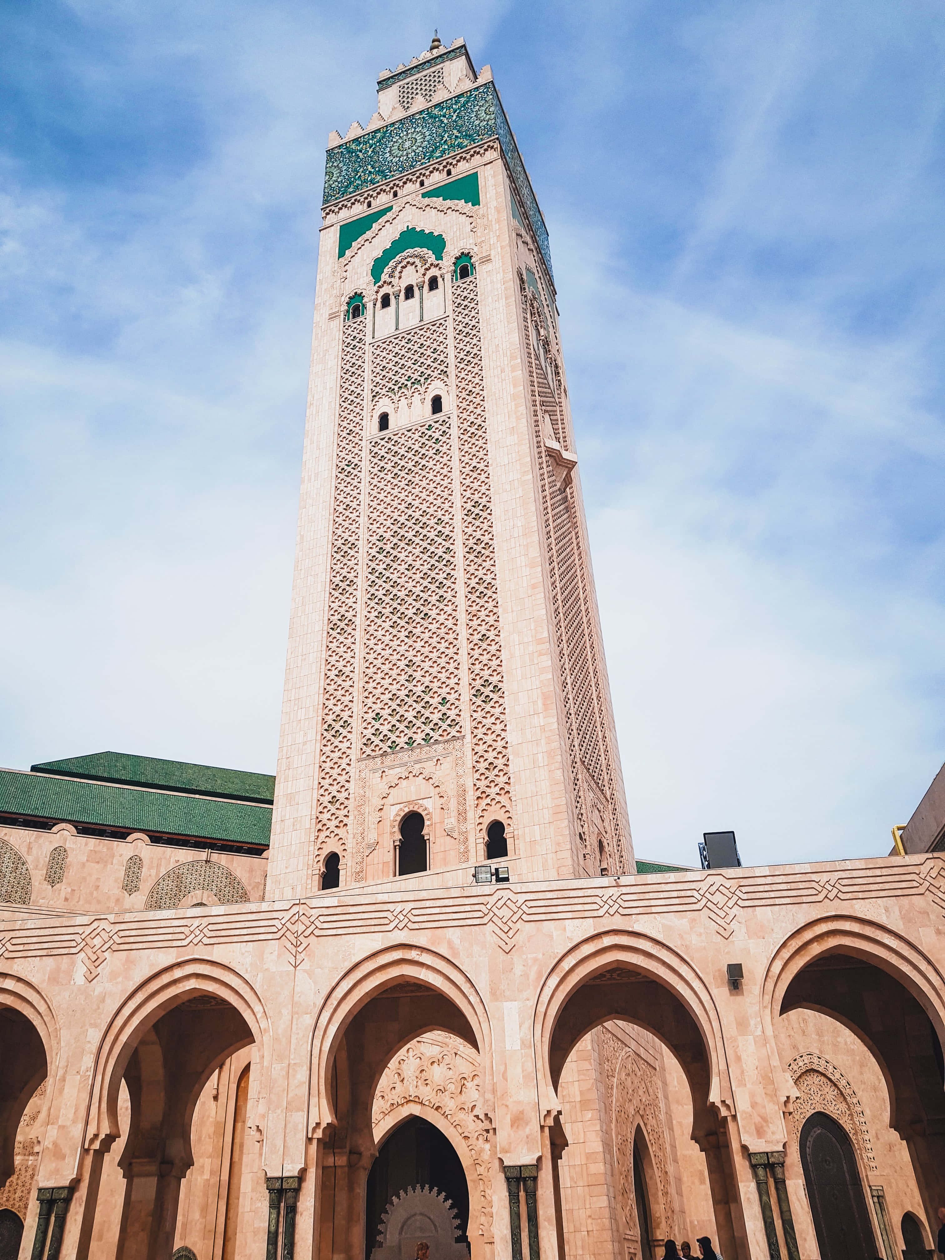 Mosque 桌布 壁紙 — 一座高聳的宣禮塔，帶有複雜的幾何圖案和綠色瓷磚點綴，在明亮的藍天和縷縷白雲襯托下巍然聳立。