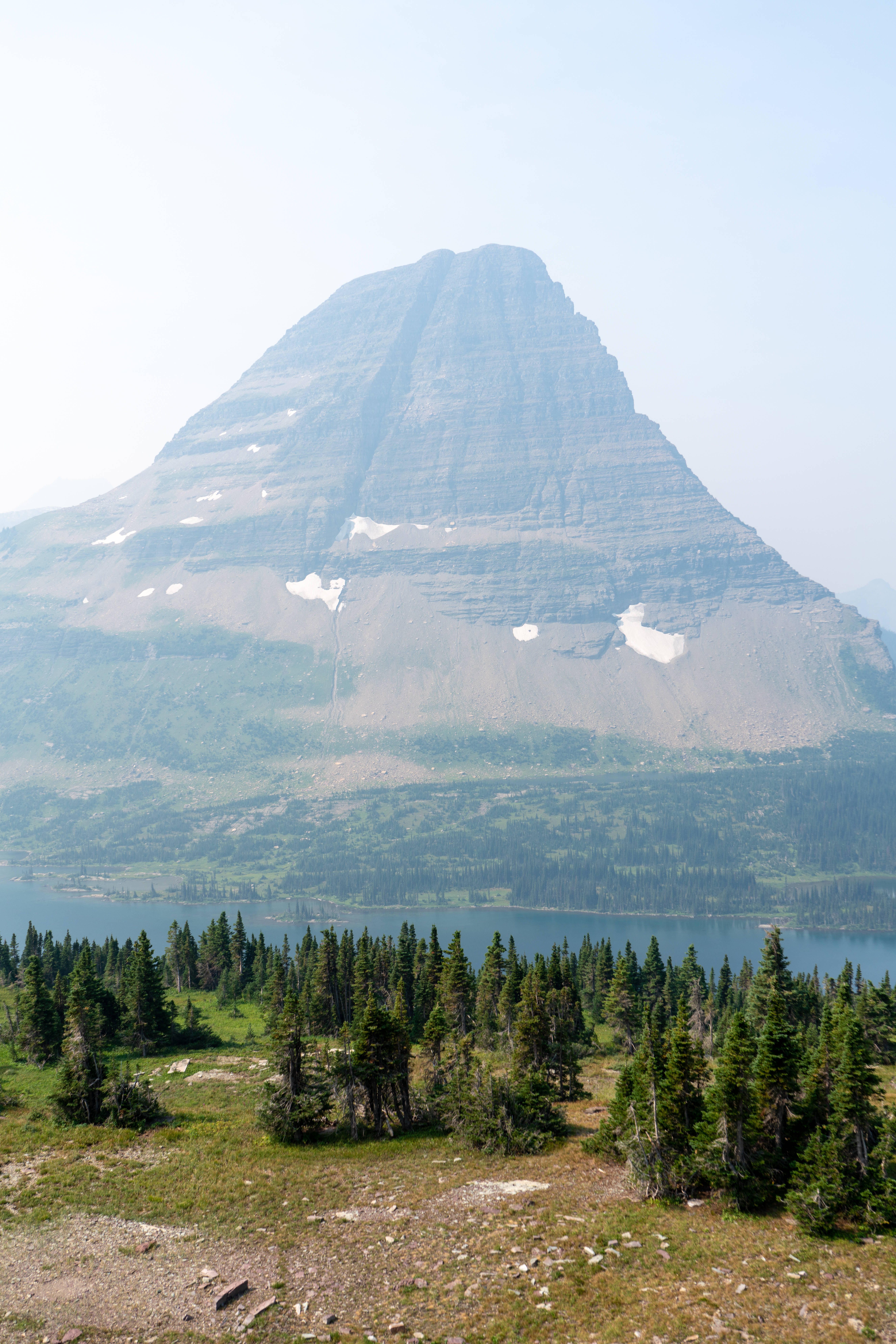 Montana 桌布 壁紙 — 一座高聳的層疊山峰，點綴著片片積雪，俯瞰著被茂密常綠森林環繞的寧靜湖泊。