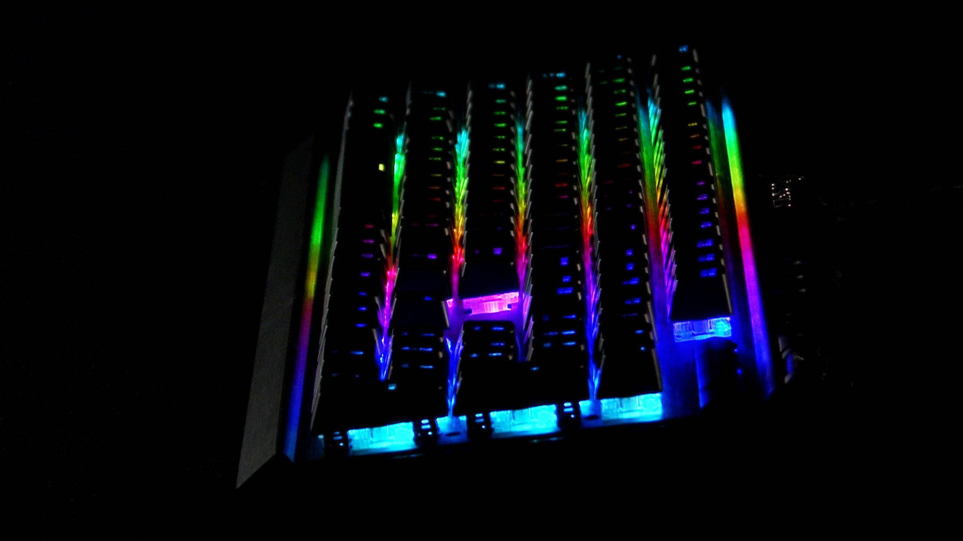 RGB 桌布 壁紙 — 一座高聳的建築物在夜晚被鮮豔的彩虹燈光照射，燈光沿著其外牆傾瀉而下，背景是漆黑的天空。