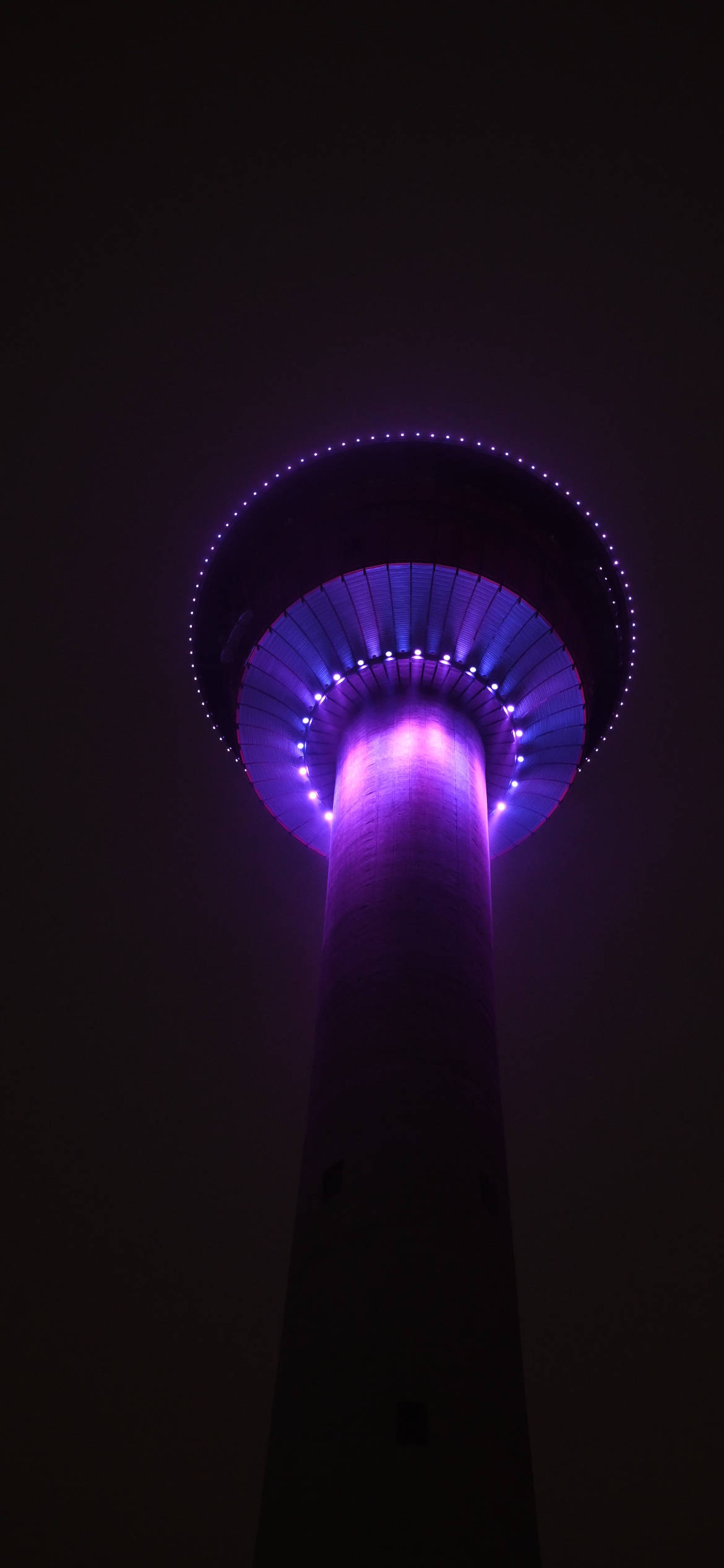 iPhone 桌布 壁紙 — 一座高聳的建築物在漆黑的夜空中被鮮豔的紫色燈光照亮。