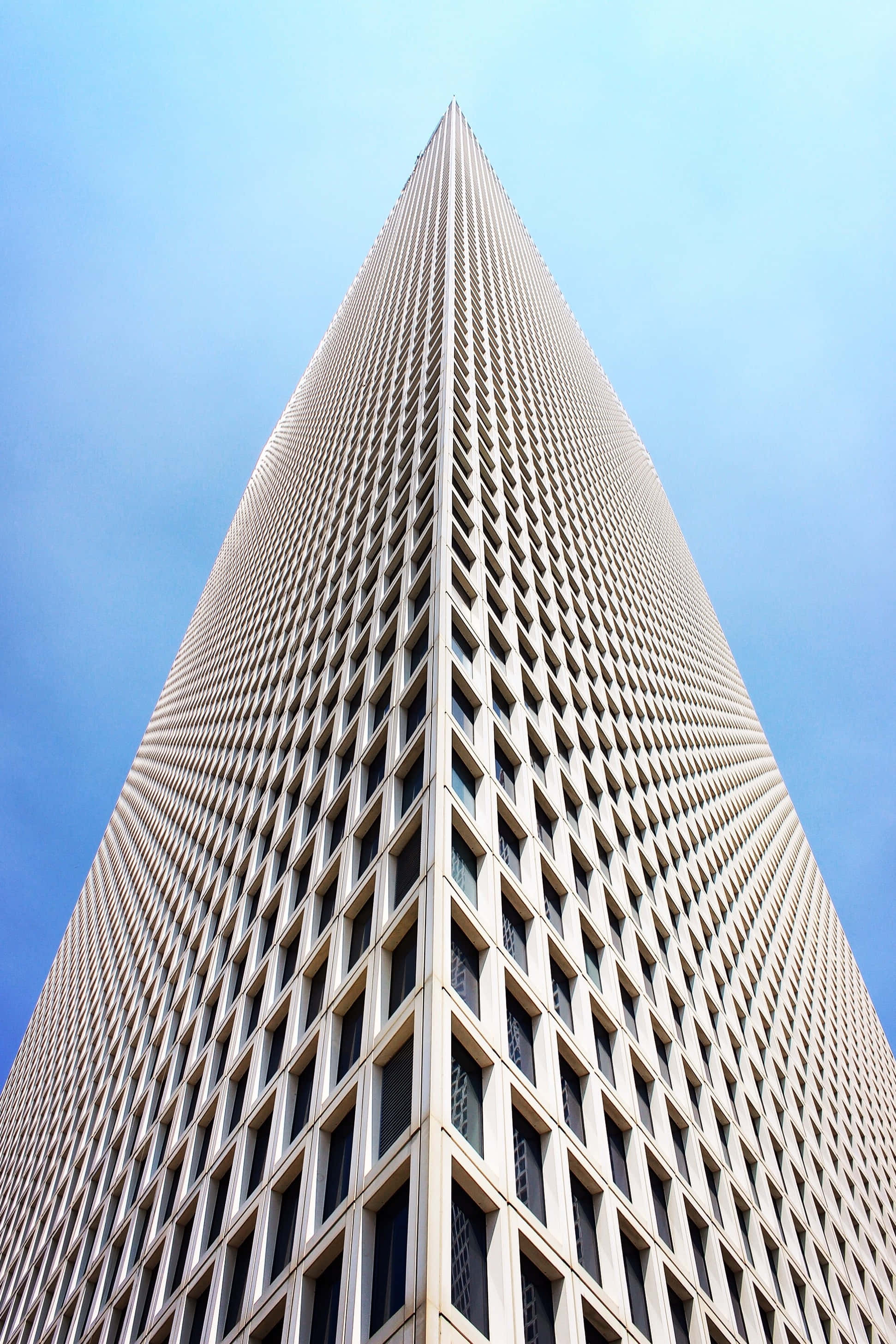 Building 桌布 壁紙 — 一座高聳的摩天大樓，其幾何網格外牆在戲劇性的低角度拍攝中刺穿清澈的藍天。