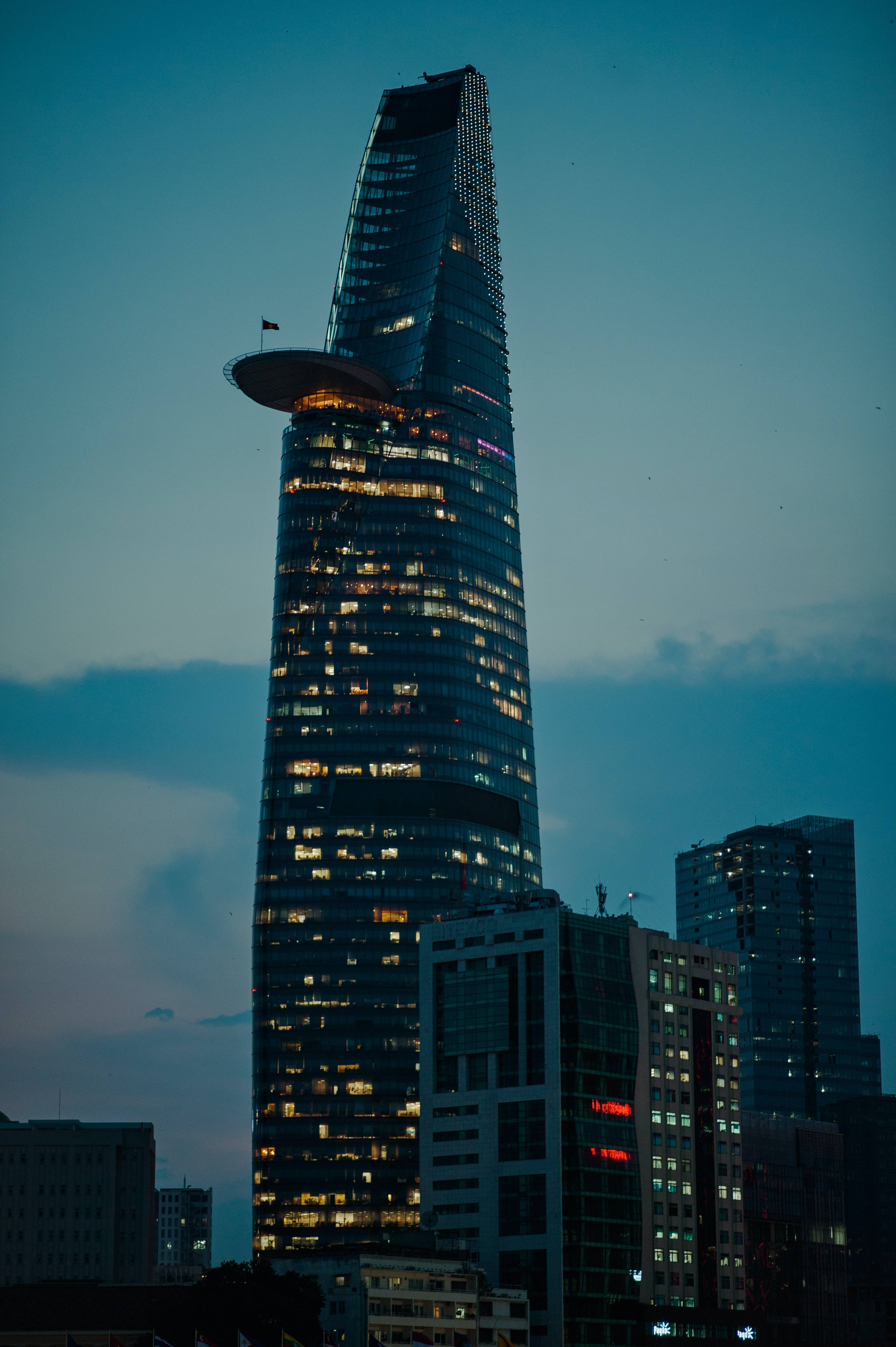 Ho Chi Minh City 桌布 壁紙 — 一座高聳的摩天大樓，帶有發光的窗戶和獨特的圓形頂部，矗立在深藍色的天空下，構成城市景觀。