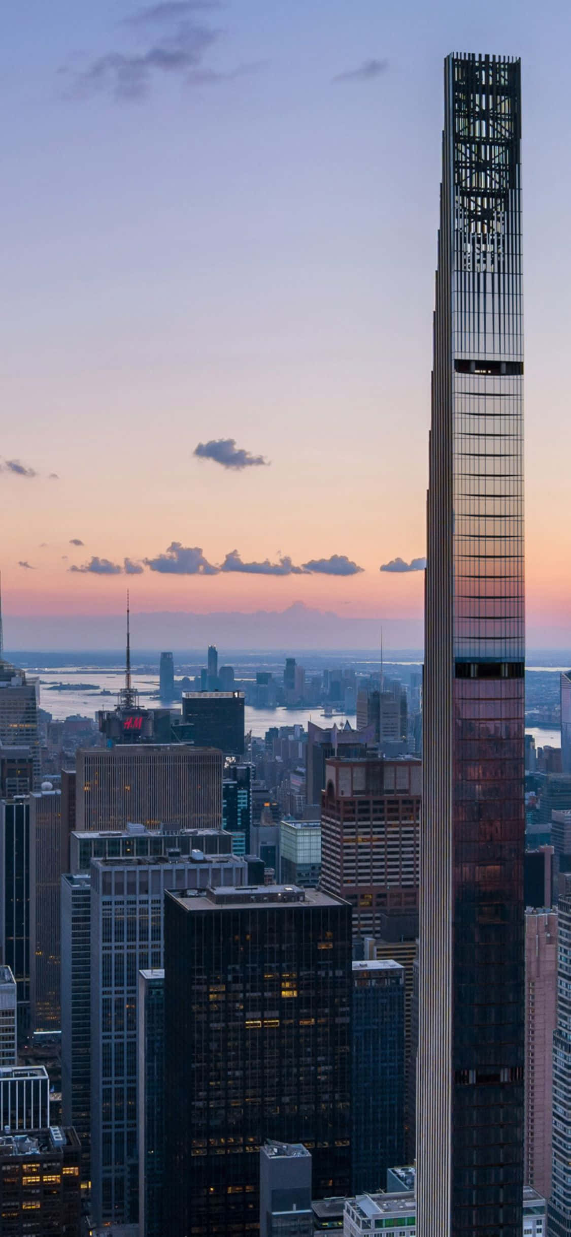 iPhone X New York 桌布 壁紙 — 一座高聳的摩天大樓在暮色中主宰著城市景觀，上方是溫暖的粉紅色和紫色天空。