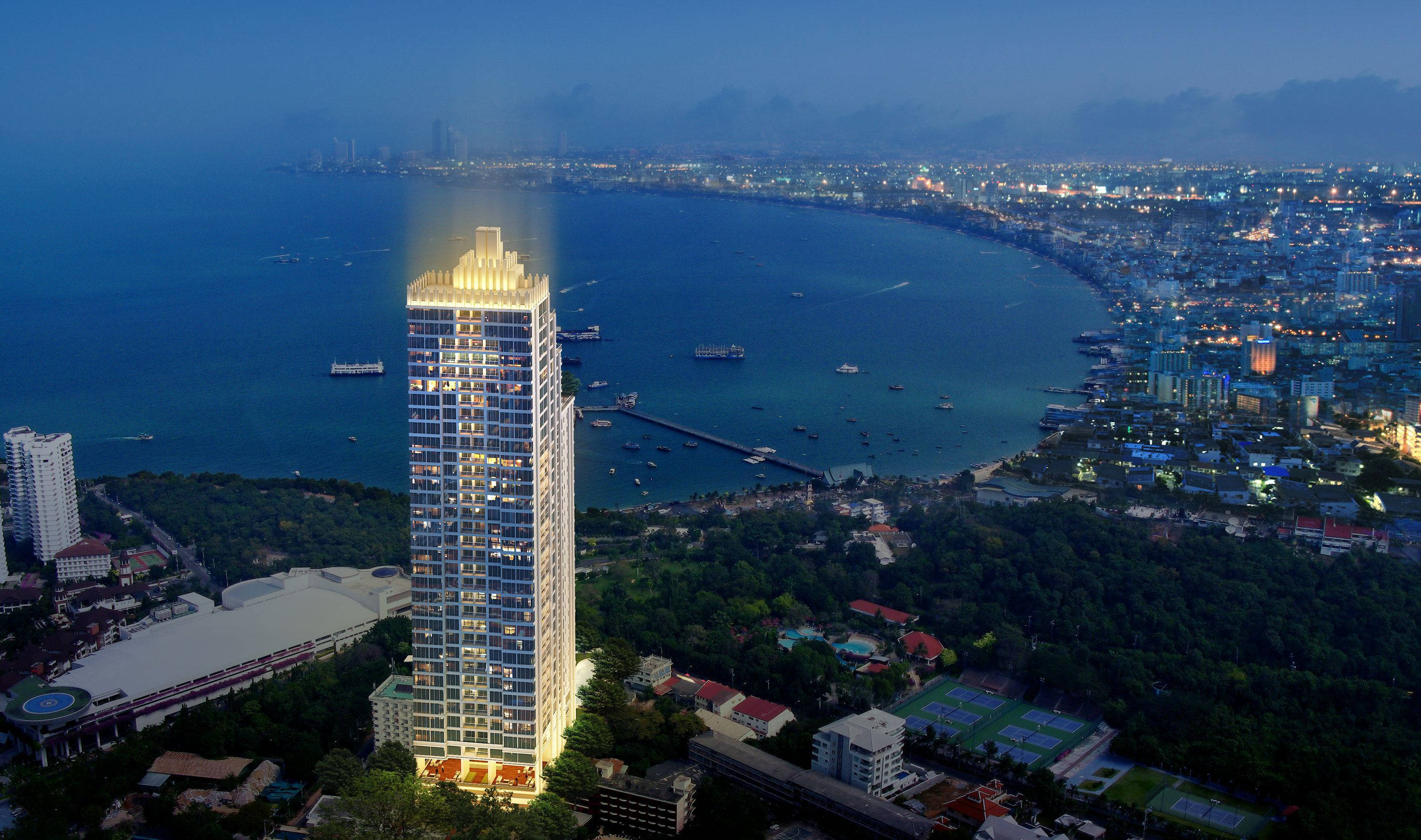Skyscraper 桌布 壁紙 — 一座高聳的摩天大樓在暮色中溫暖地發光，俯瞰著繁華的海濱城市和點綴著船隻的深藍色大海。