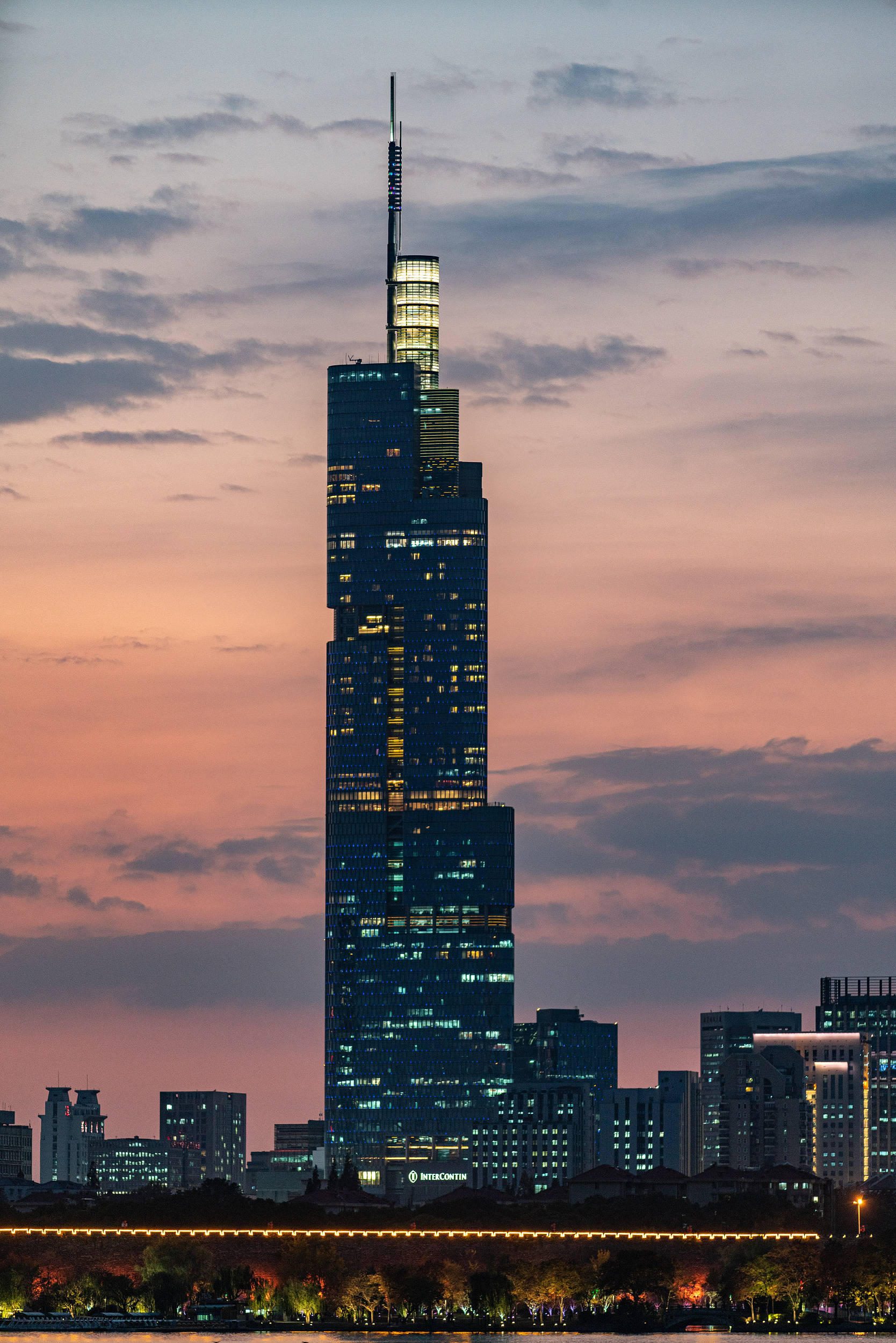 Buildings 桌布 壁紙 — 一座高聳的摩天大樓在暮色天空中閃耀，天空被柔和的粉紅色和紫色雲彩渲染。