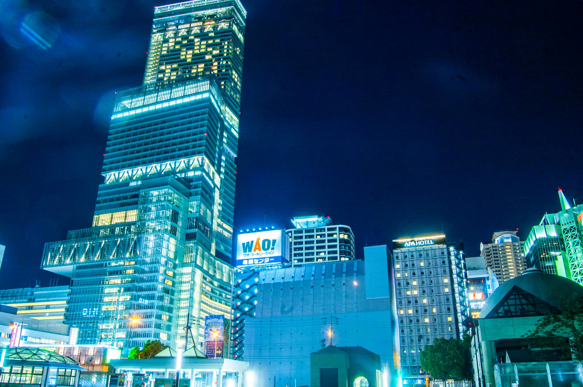 一座發光的摩天大樓主宰著充滿活力的城市夜景，周圍建築物燈火通明。