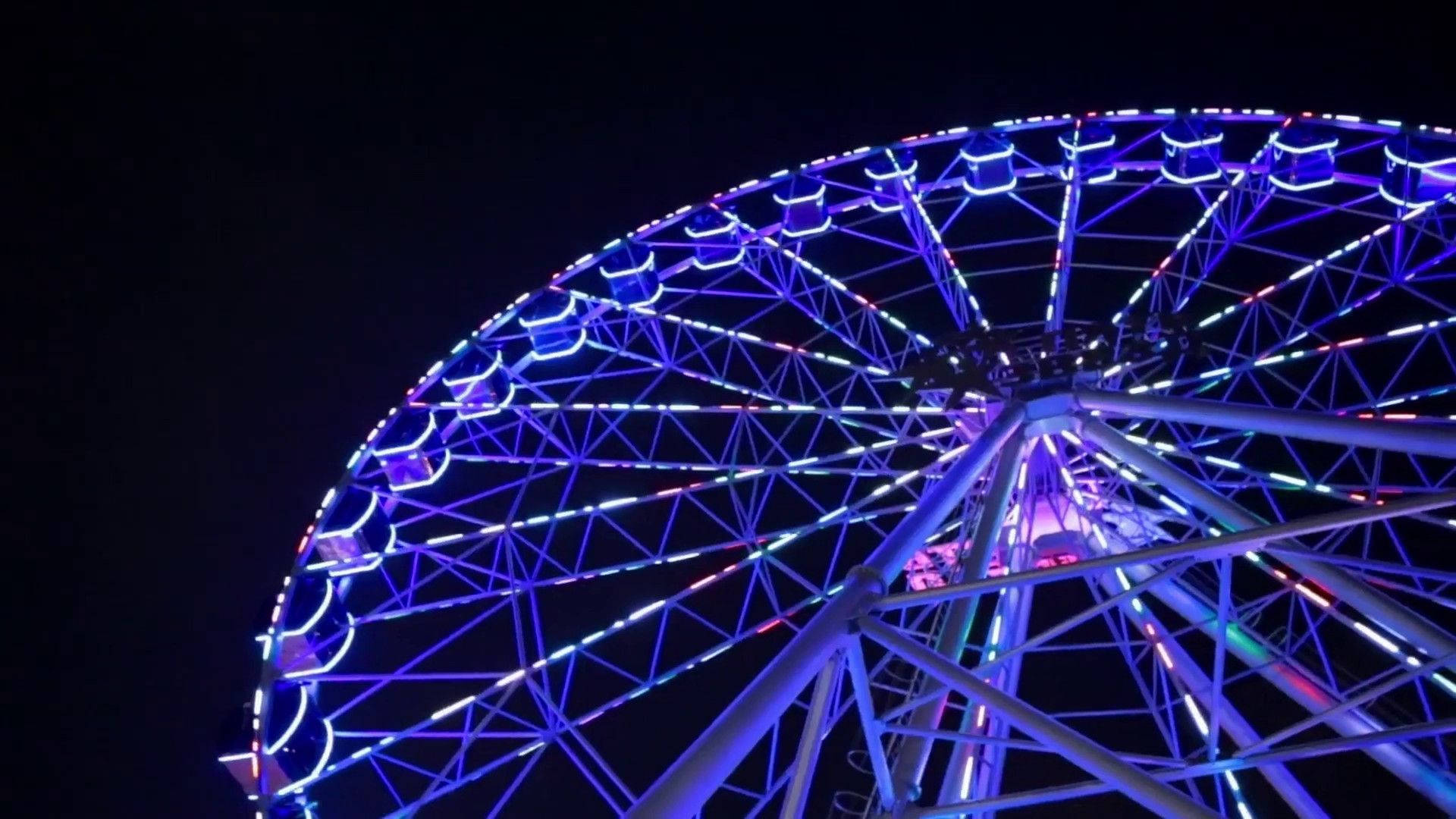 blue aesthetic pc 桌布 壁紙 — 一座高聳的摩天輪在漆黑的夜空中閃耀著鮮豔的藍色和紫色燈光。