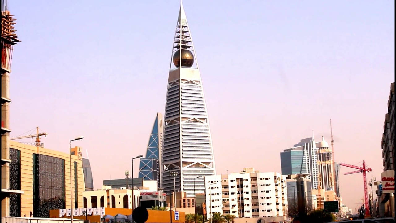 Riyadh 桌布 壁紙 — 一座高聳的未來主義摩天大樓，頂部有一個金色球體，在日落時分點綴著繁華的城市天際線。