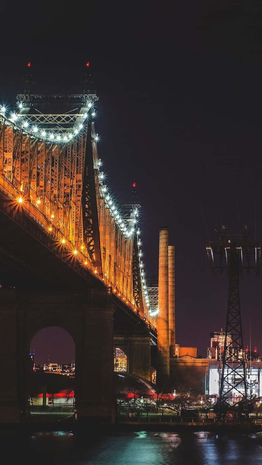 Nyc Aesthetic 桌布 壁紙 — 一座高聳的橋樑被金色燈光照亮，在無星的夜空下倒映在黑暗的水面上。
