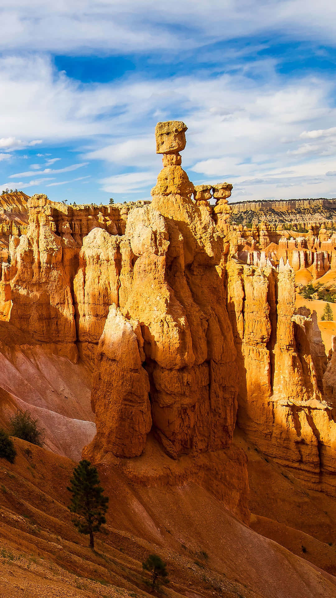 National Parks 桌布 壁紙 — 一座高聳的橙色岩柱在布萊斯峽谷中矗立，猶如哨兵，背景是明亮藍天和縷縷白雲。