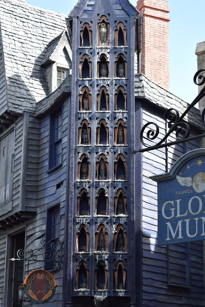 The Hogwarts Owlery 桌布 壁紙 — 一座高聳的深藍色哥德式塔樓，帶有拱形壁龕，內有貓頭鷹雕像，矗立於經風吹日曬的木造建築上，在明亮的日光下。