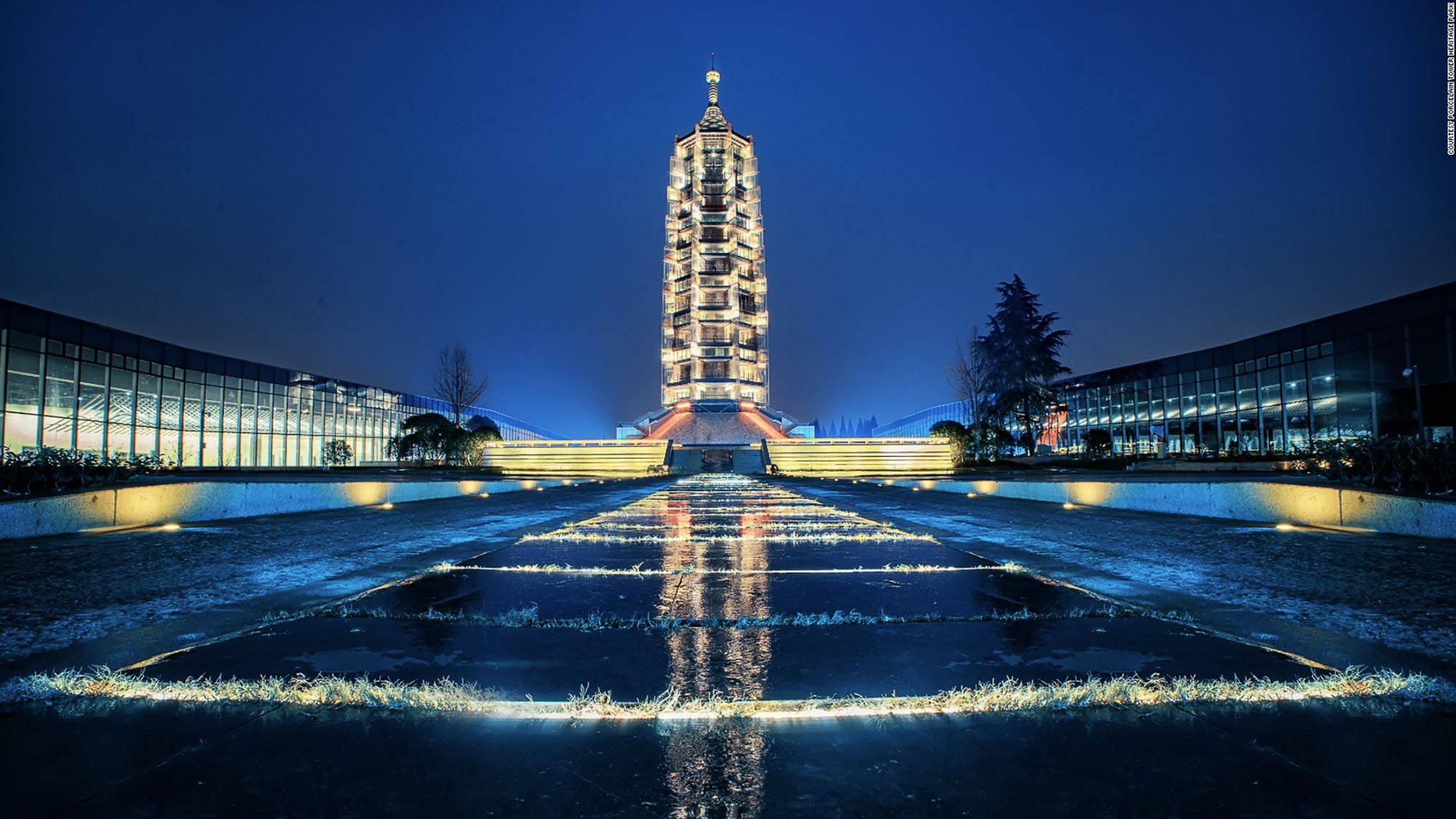 Nanjing 桌布 壁紙 — 一座高聳的燈光寶塔在夜晚巍然聳立，燈光完美地反射在帶有幾何水景的濕潤廣場上。