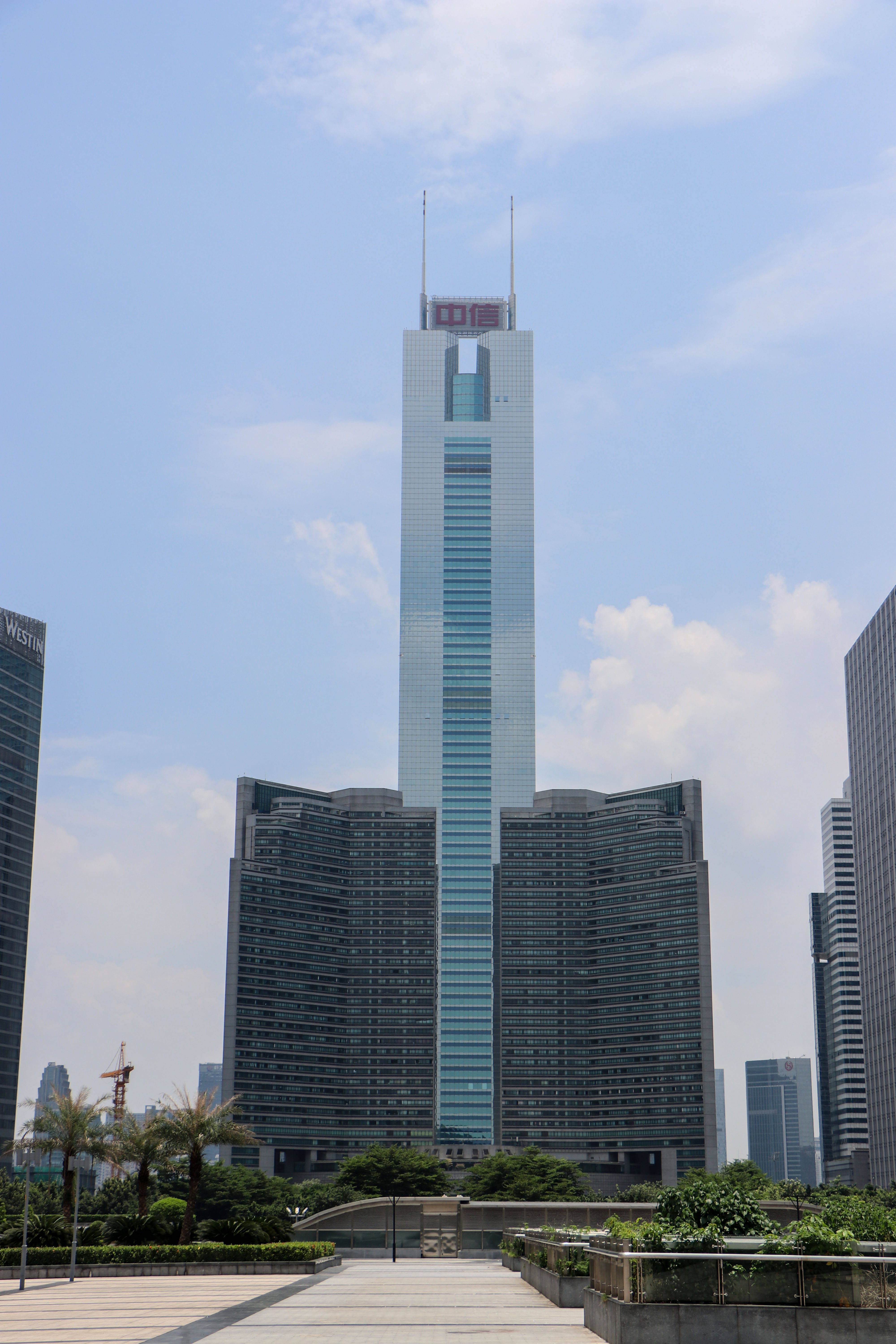 Guangzhou 桌布 壁紙 — 一座高聳的玻璃摩天大樓，帶有「中信」標誌，在明亮的藍天和散落的雲朵下，聳立於周圍的現代建築之上。