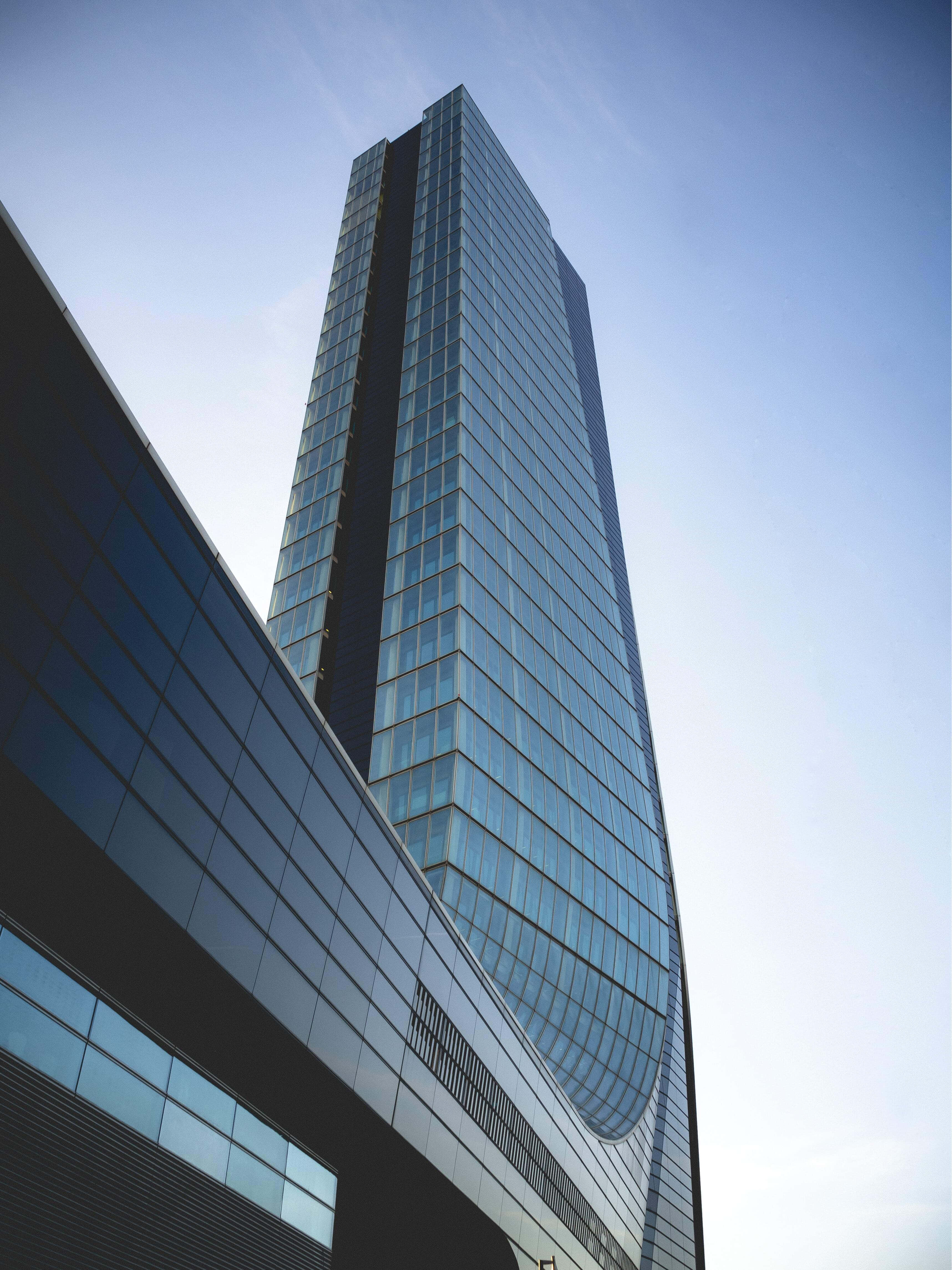 Building 桌布 壁紙 — 一座高聳的玻璃摩天大樓，帶有弧形外牆，在清澈的藍天下崛起，其反射表面映照著天空和周圍的建築物。
