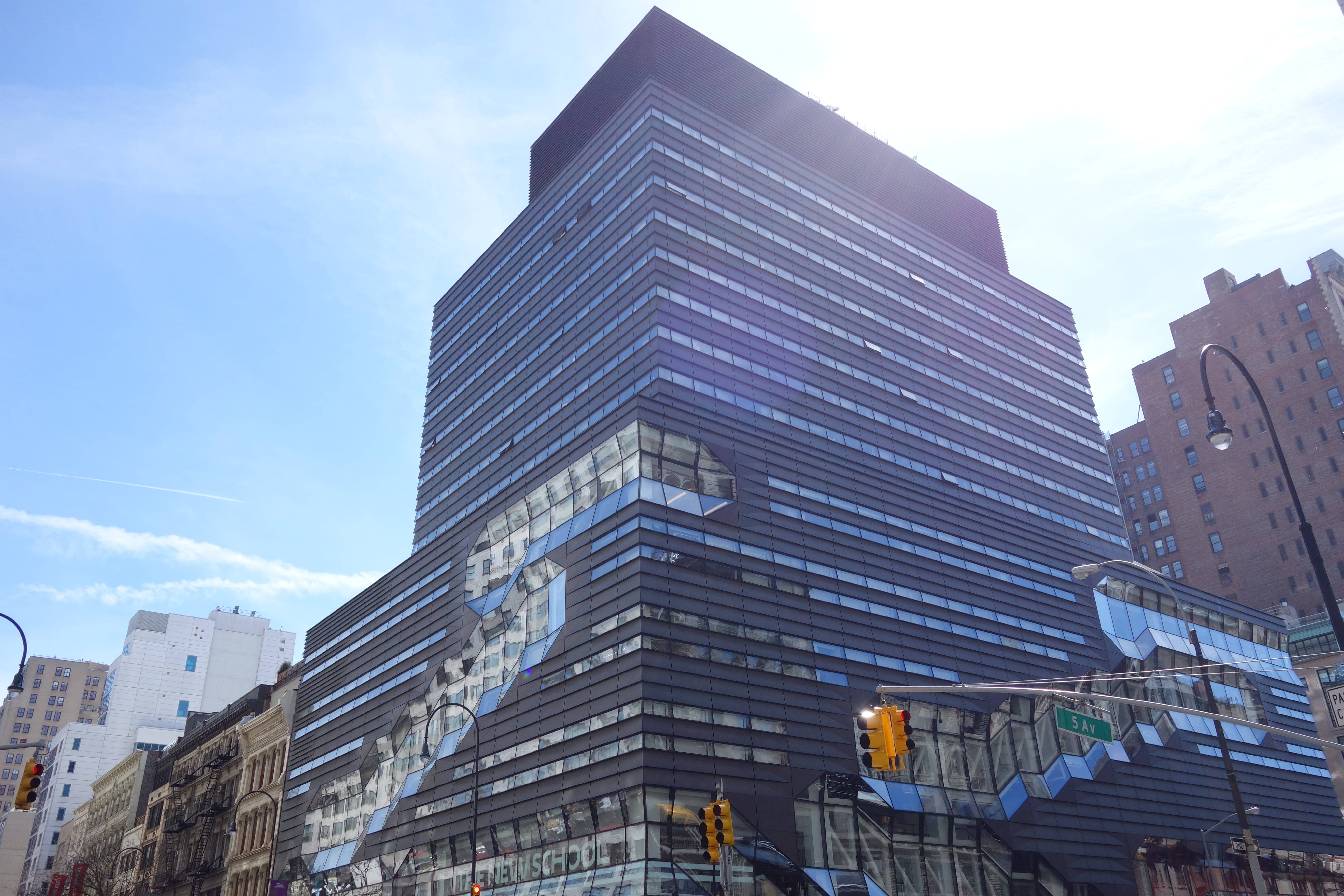 Building 桌布 壁紙 — 一座高聳的玻璃摩天大樓，幾何外牆反射著明亮的藍天和周圍的城市景觀。
