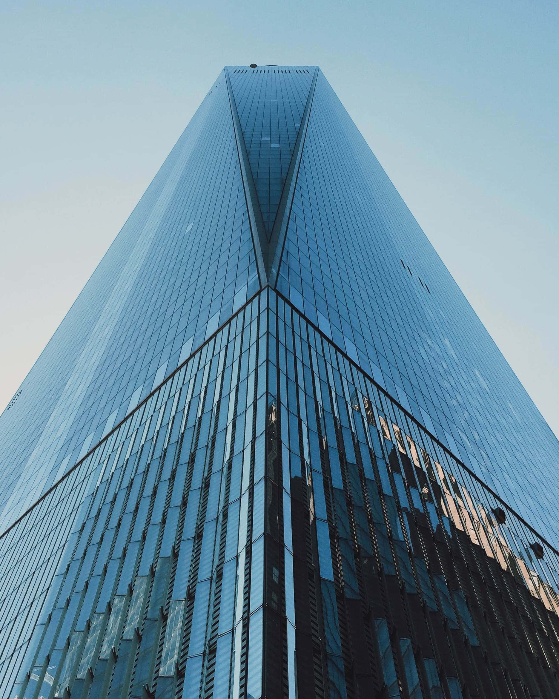 Building 桌布 壁紙 — 一座高聳的玻璃摩天大樓以其銳利的幾何線條和反光外牆刺穿清澈的藍天。