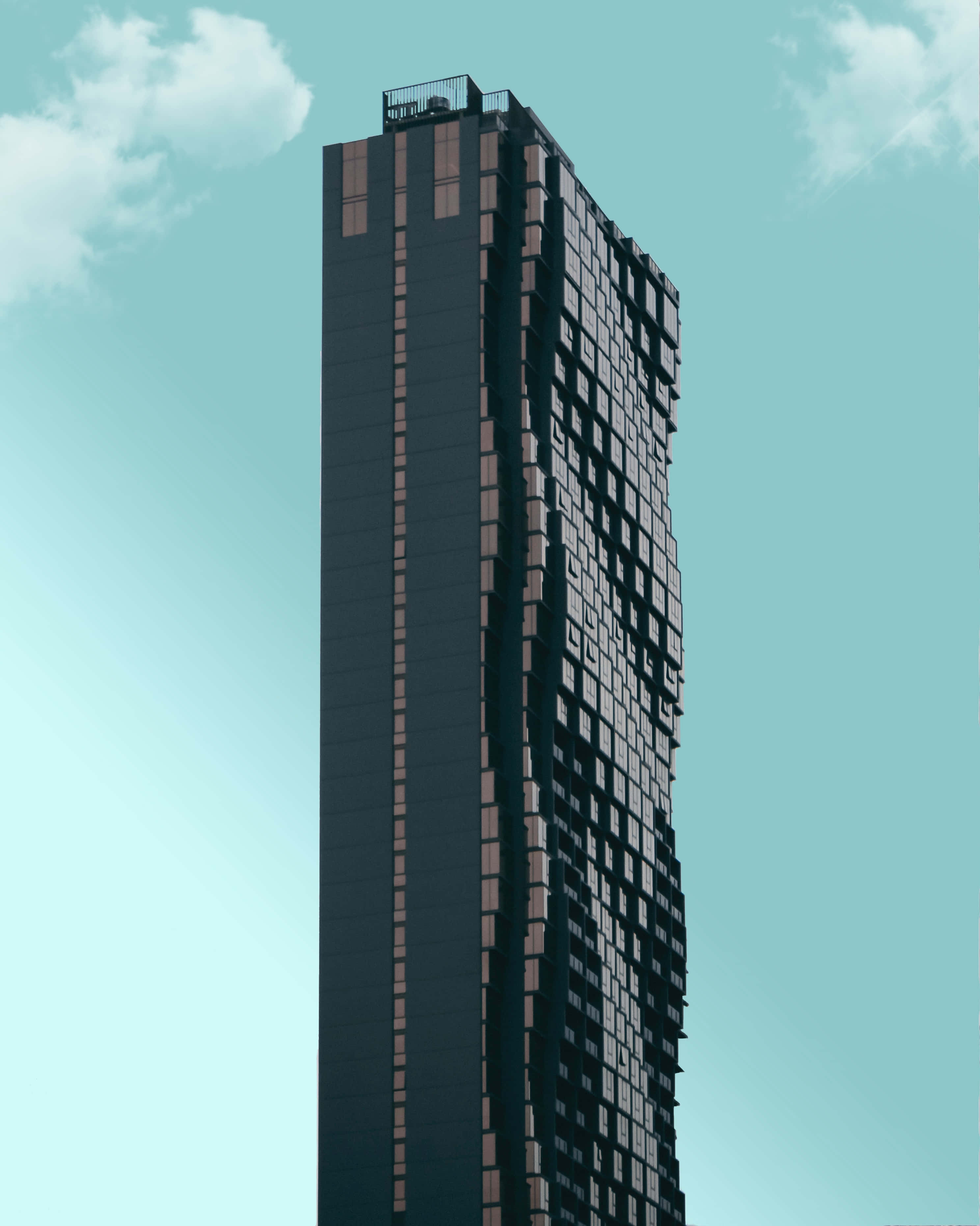Building 桌布 壁紙 — 一座高聳的現代摩天大樓，帶有像素化外牆，在晴朗的藍綠色天空和 fluffy 白雲襯托下矗立。