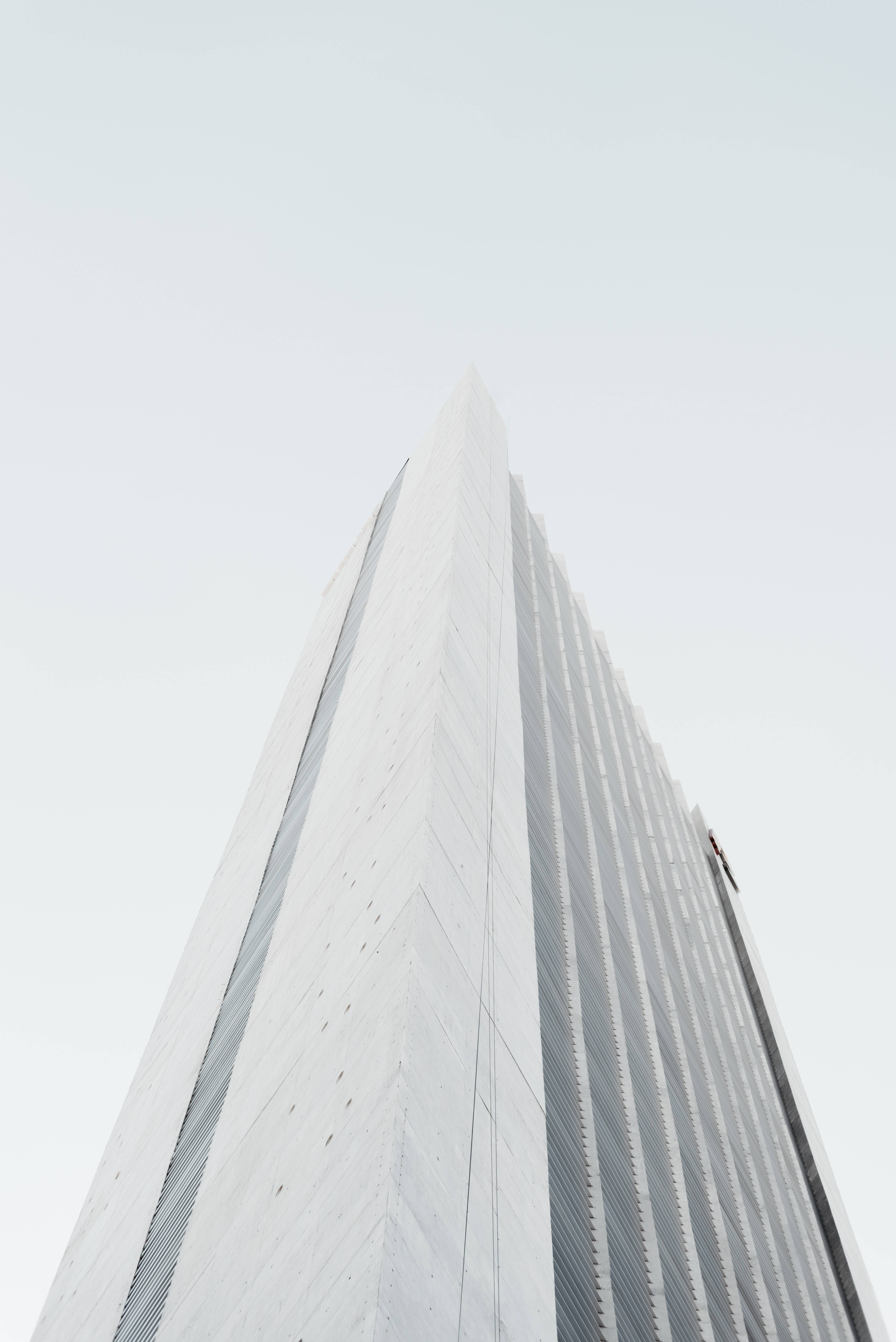 Building 桌布 壁紙 — 一座高聳的現代摩天大樓，帶有銳利的幾何線條，在蒼白的陰天中升起。