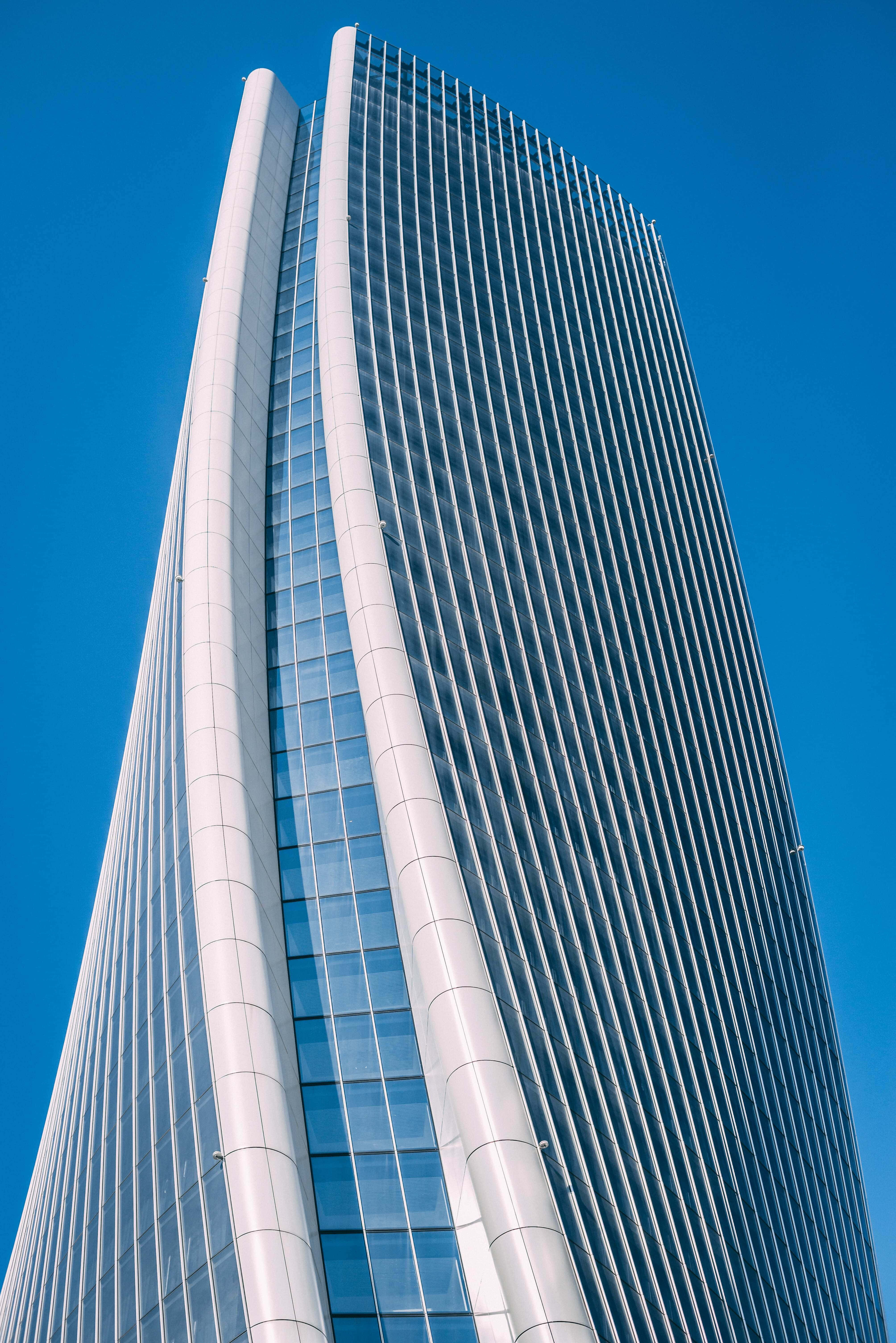 Building 桌布 壁紙 — 一座高聳的現代摩天大樓，採用弧形玻璃和白色面板，在清澈的藍天下拔地而起。