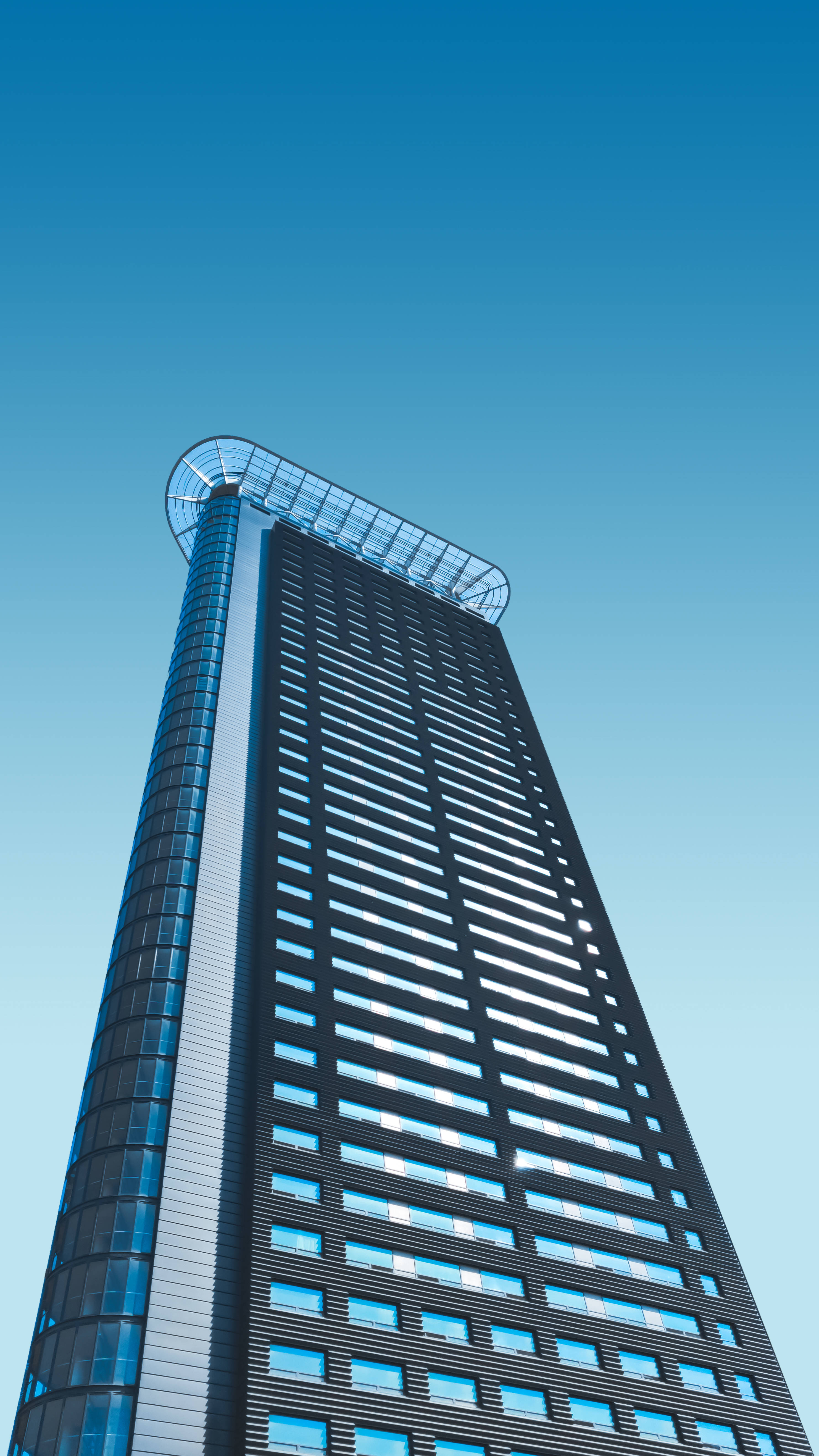 Skyscraper 桌布 壁紙 — 一座高聳的現代摩天大樓，玻璃和鋼鐵外牆直插清澈的藍天。