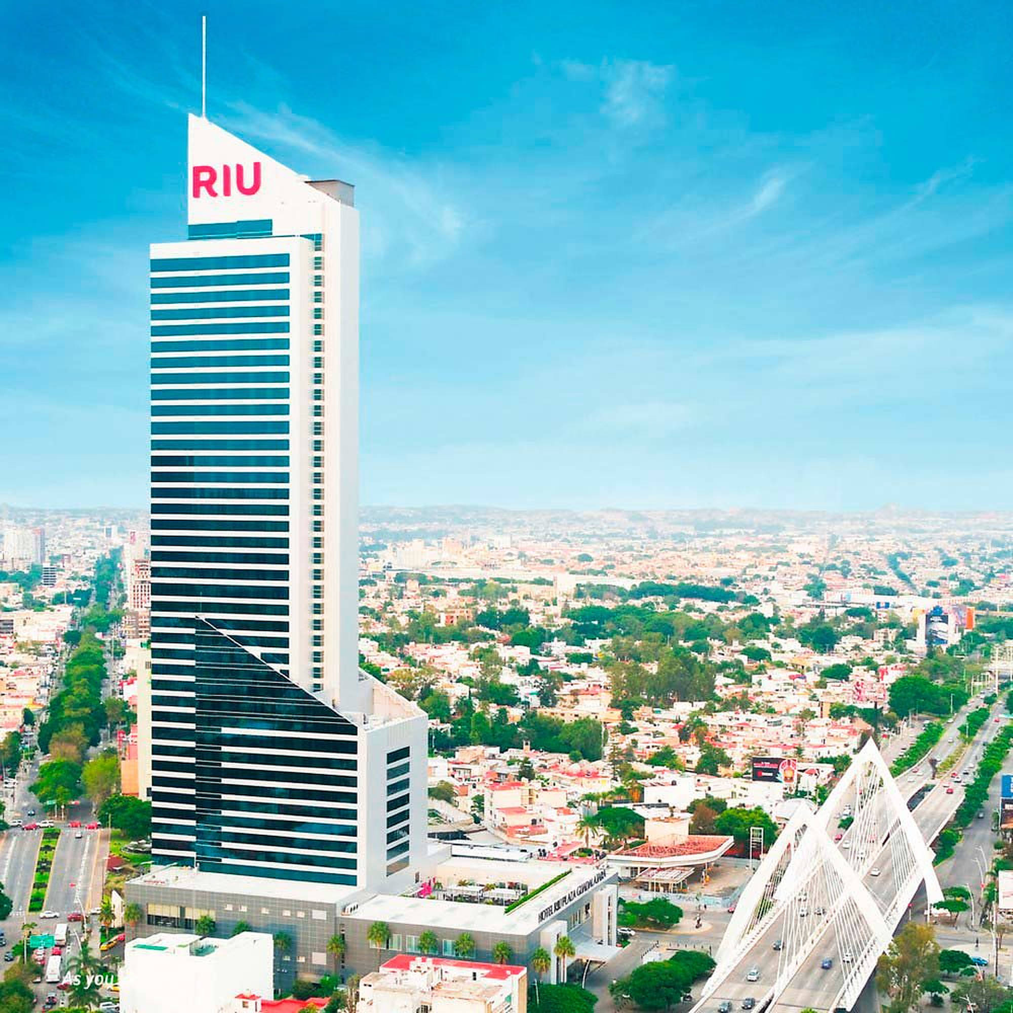 Guadalajara 桌布 壁紙 — 一座高聳的白色RIU酒店摩天大樓在晴朗的藍天和散落的雲朵下主導著充滿活力的城市景觀。