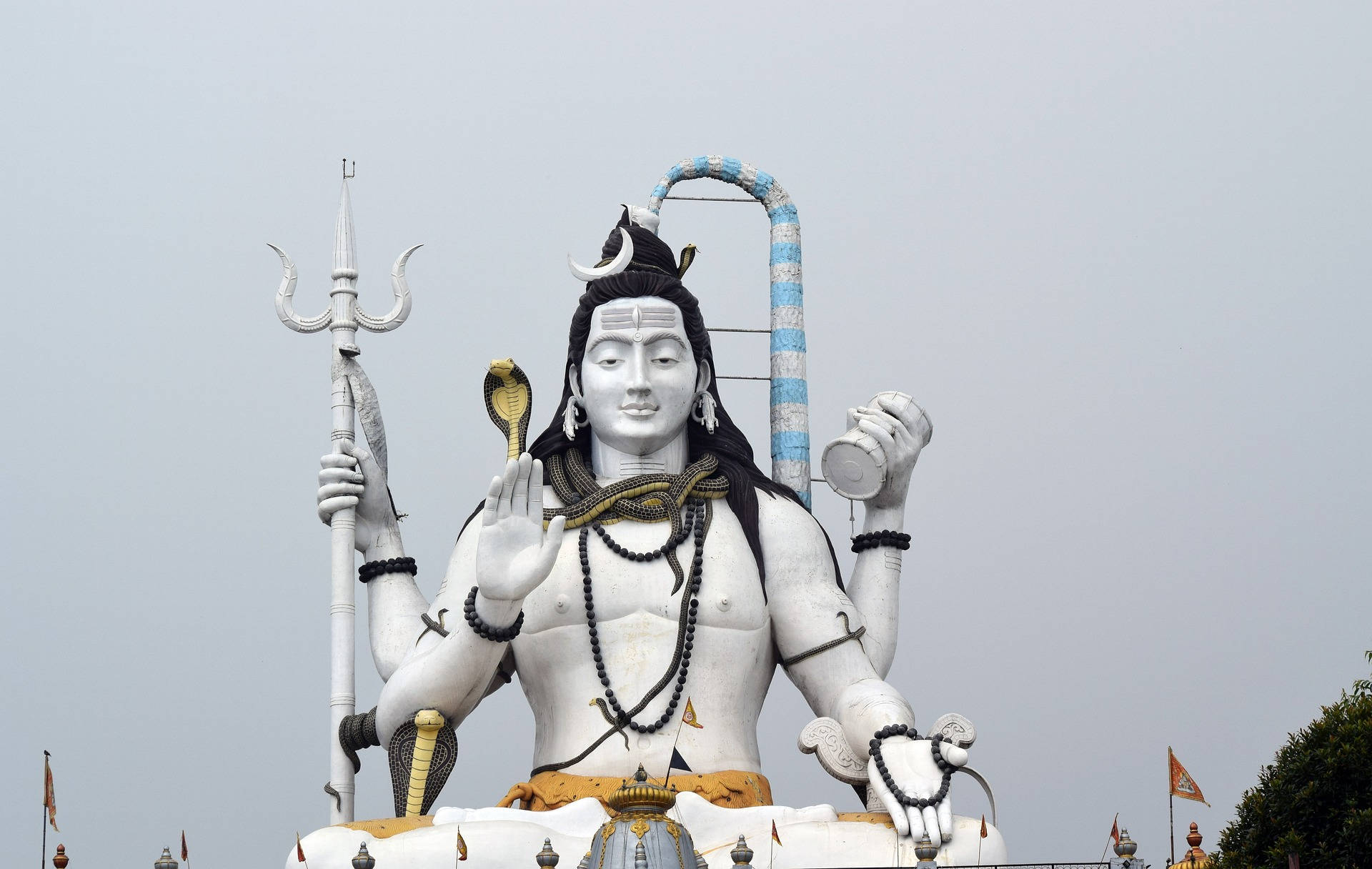 Indian 桌布 壁紙 — 一座高聳的白色濕婆神像，多臂手持三叉戟、眼鏡蛇和鼓，背景是灰色天空。