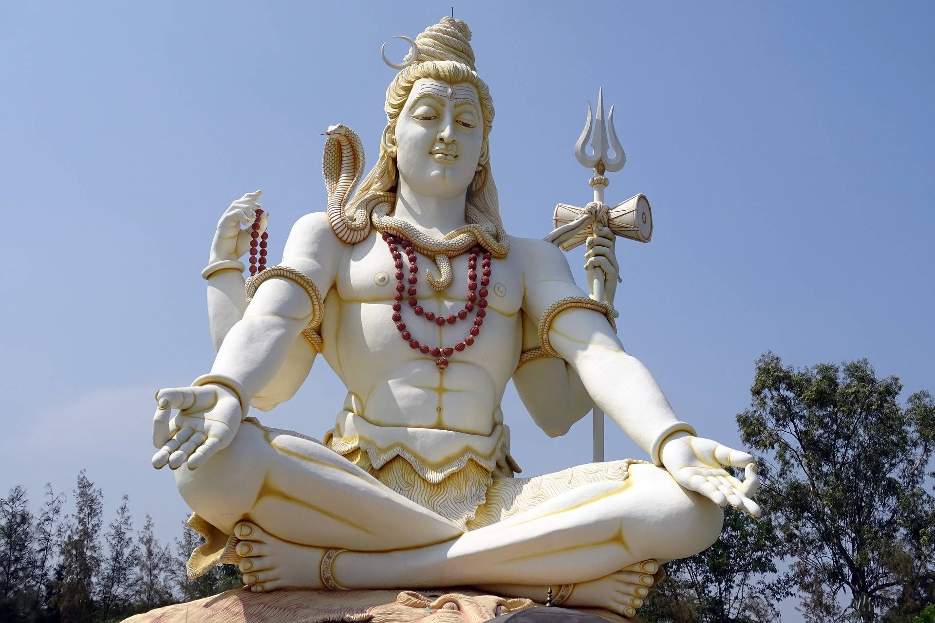 Indian 桌布 壁紙 — 一座高聳的白色石像，濕婆神在晴朗藍天下、樹木背景中寧靜冥想。