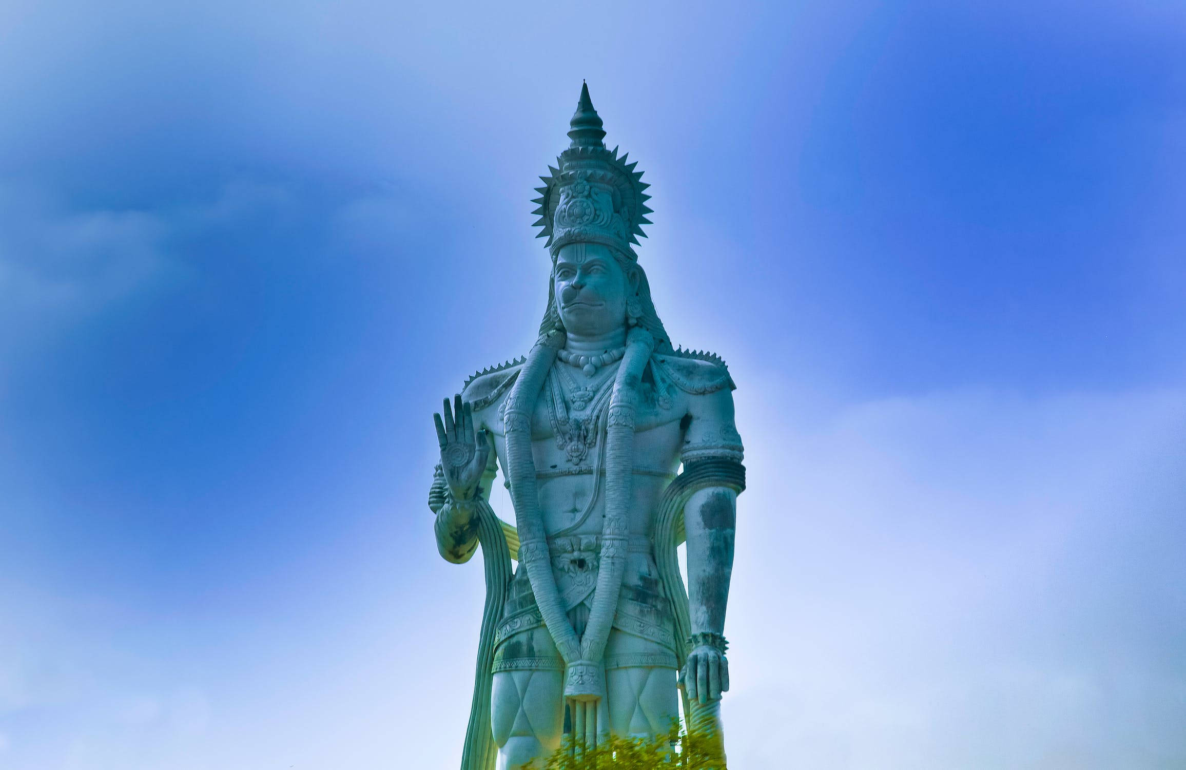 Hindu God 桌布 壁紙 — 一座高聳的白色神像，戴著精緻的皇冠和珠寶，矗立在藍天白雲下。