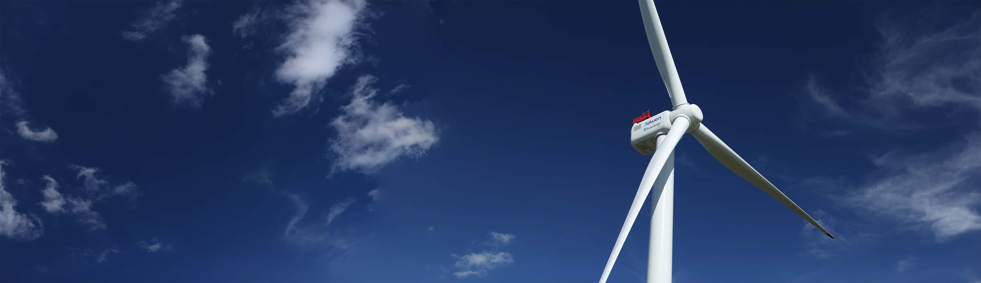 Wind 桌布 壁紙 — 一座高聳的白色風力渦輪機矗立在點綴著縷縷白雲的湛藍天空下。