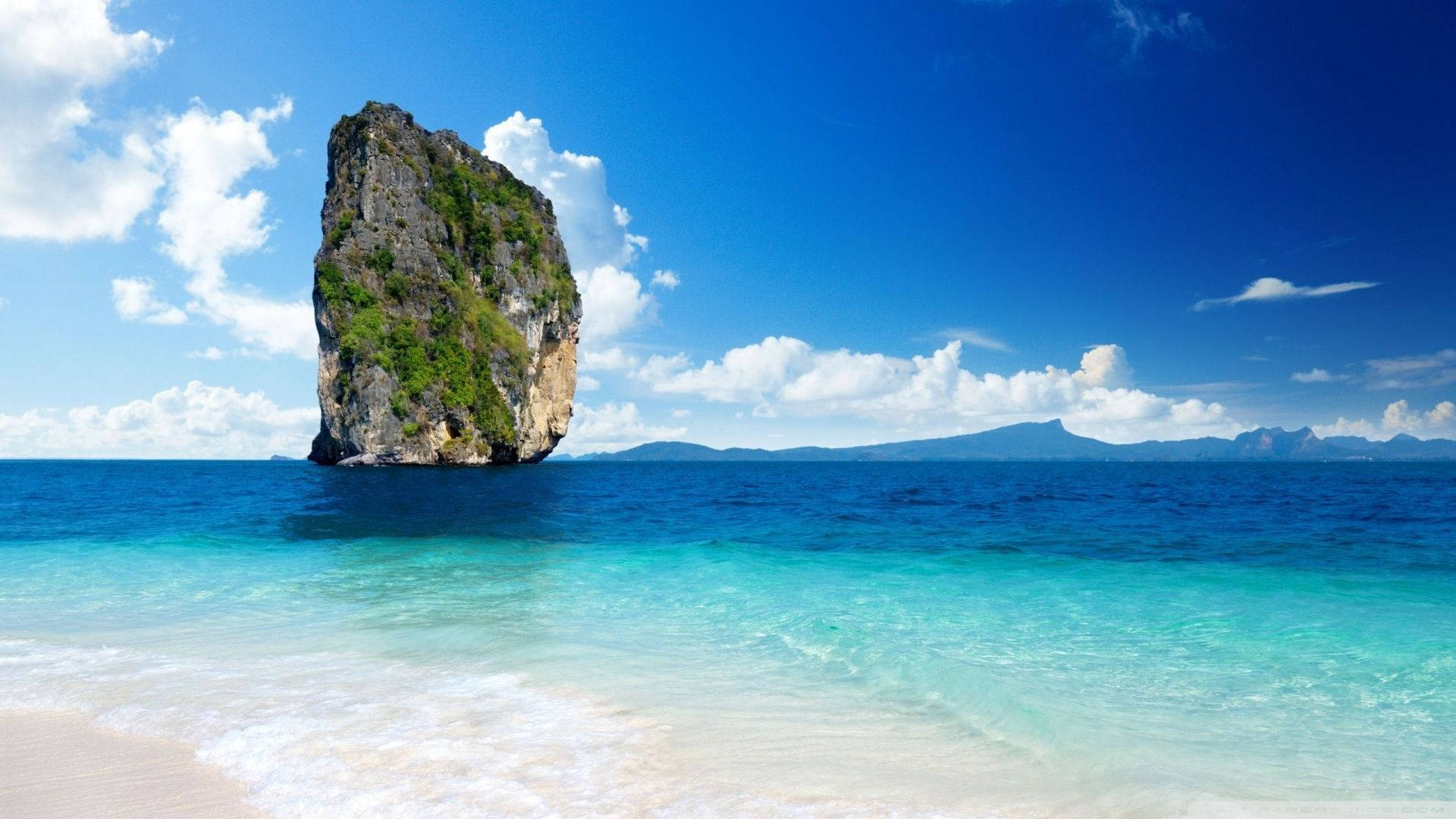 Palau 桌布 壁紙 — 一座高聳的石灰岩從清澈碧綠的海水中升起，旁邊是白色沙灘，上方是晴朗的藍天和白雲。