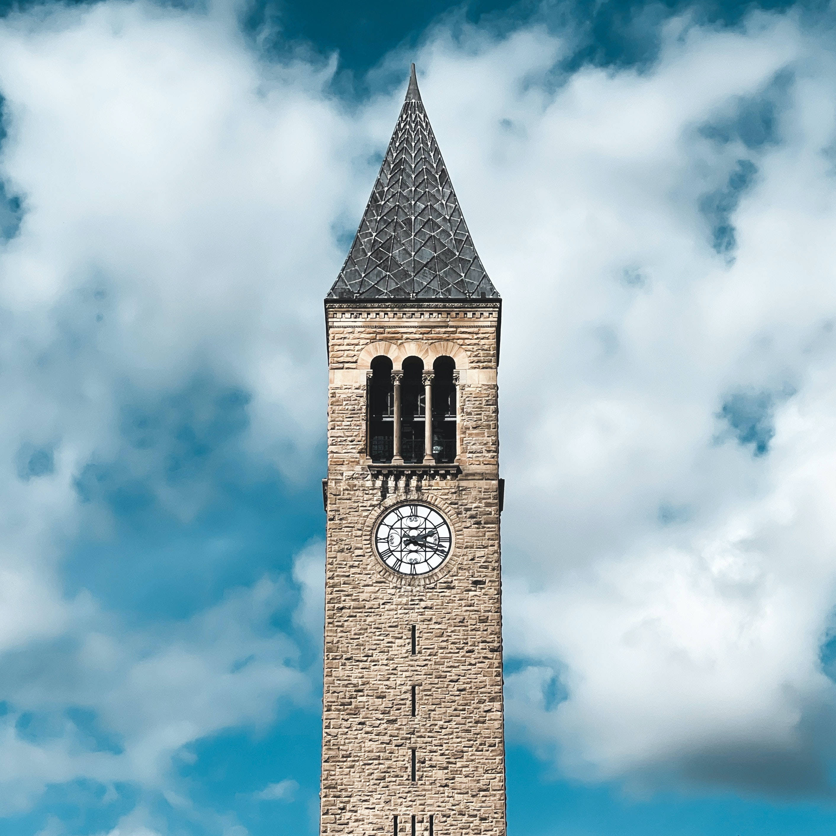 Clock 桌布 壁紙 — 一座高聳的石造鐘樓，頂部尖尖，矗立在佈滿蓬鬆白雲的明亮藍天下。