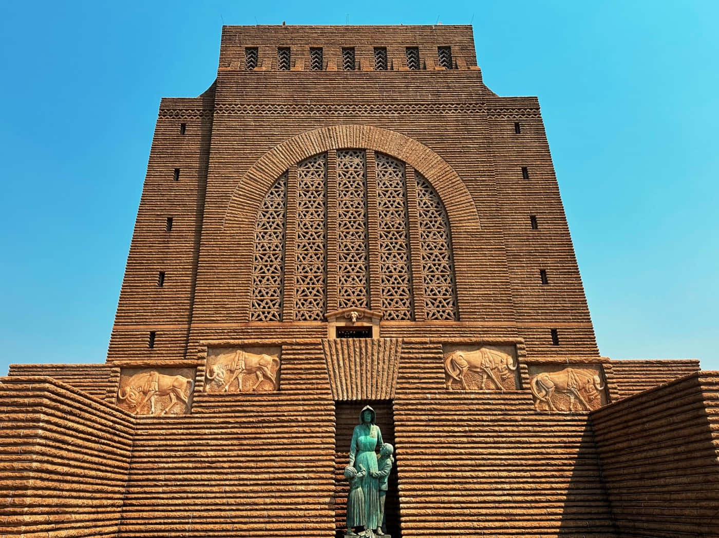 Architecture 桌布 壁紙 — 一座高聳的磚砌紀念碑，在清澈的藍天下帶有複雜的幾何圖案和公牛浮雕。