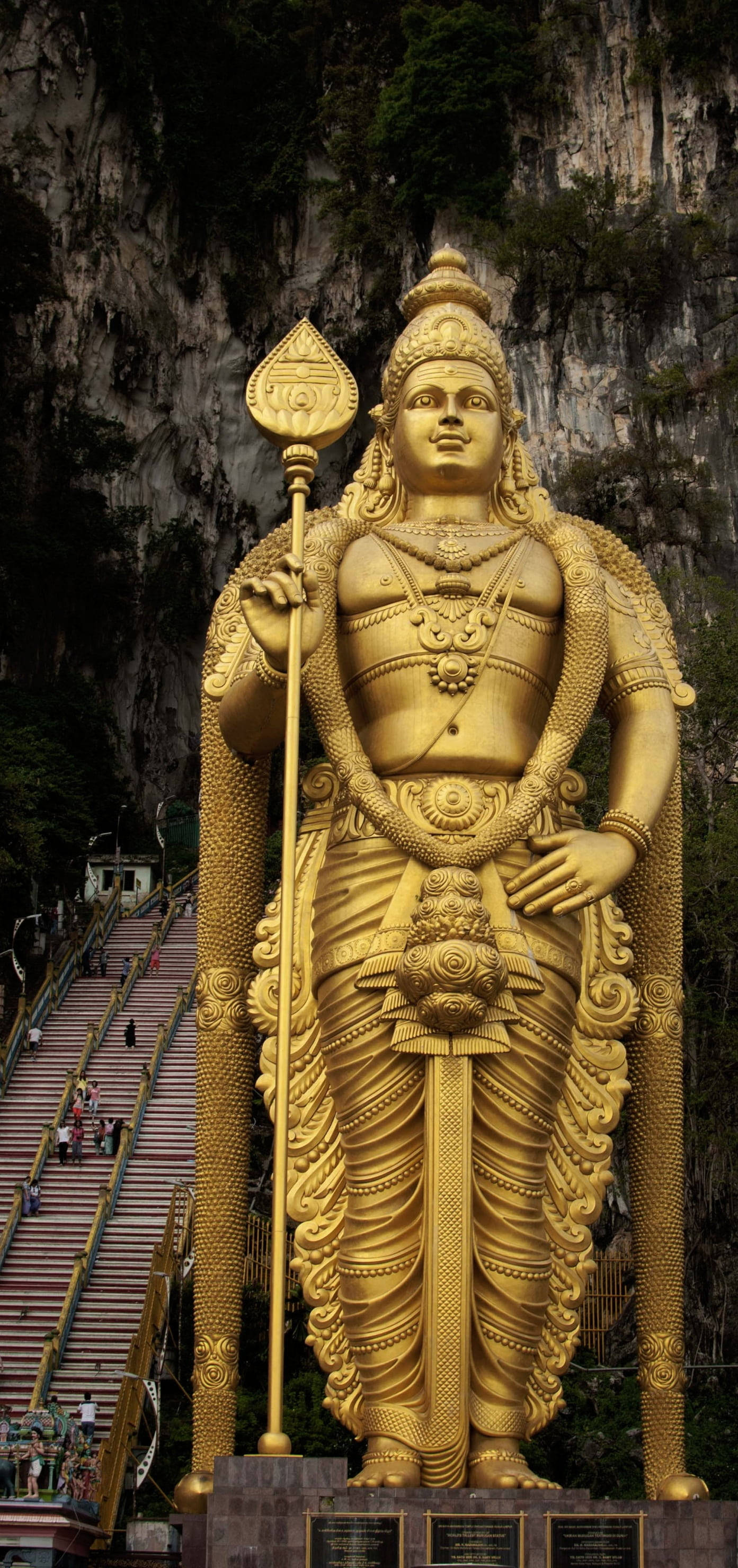 Tamil God 桌布 壁紙 — 一座高聳的穆魯甘勳爵金色雕像雄偉地矗立在翠綠懸崖的底部，一條長長的樓梯蜿蜒而上。