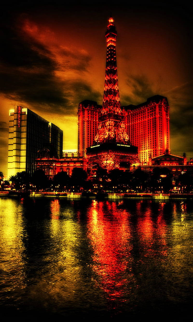 Las Vegas 桌布 壁紙 — 一座高聳的紅色發光艾菲爾鐵塔複製品在火紅的橙色天空下閃耀，其倒影在下方黑暗的水面上閃爍。