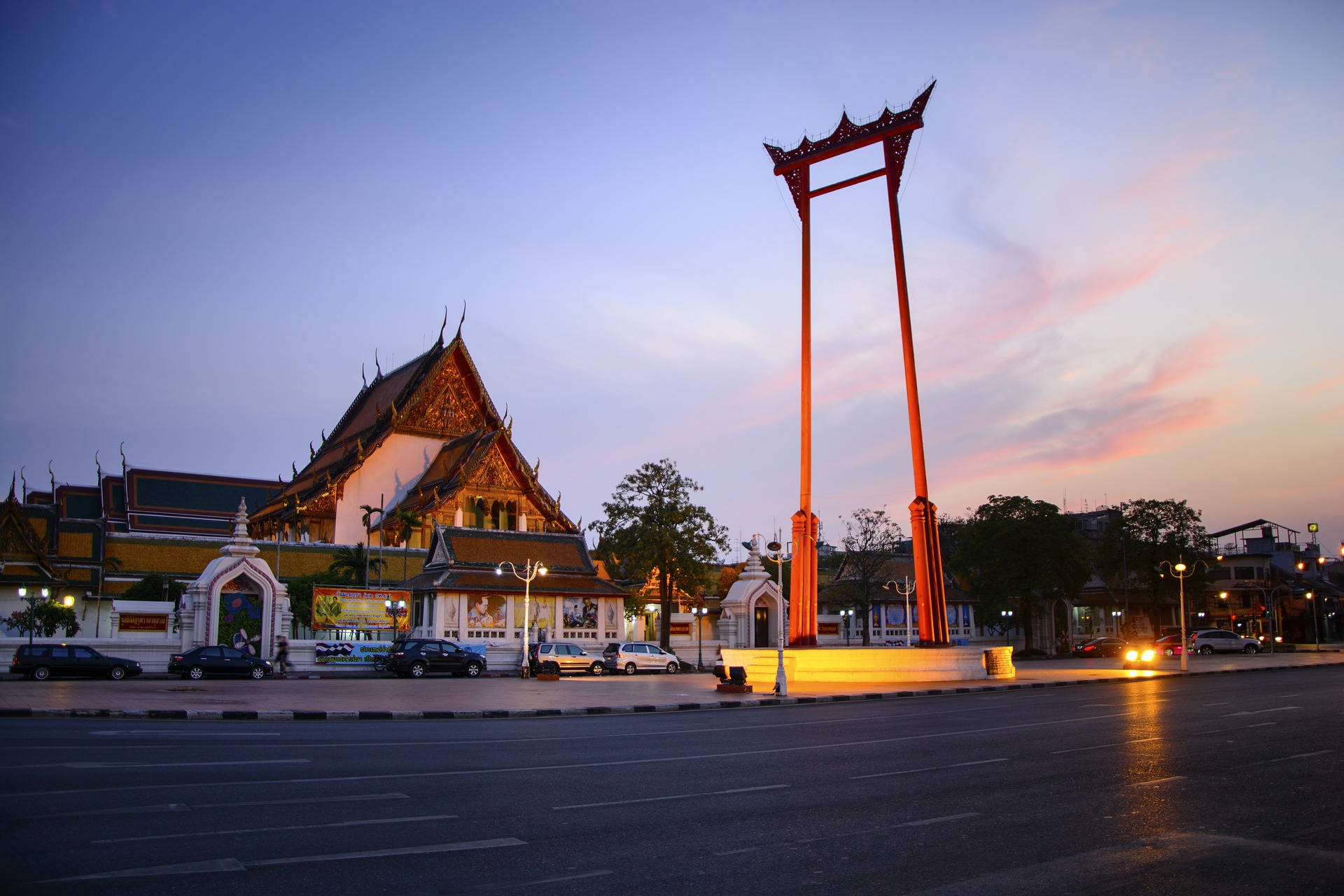 Bangkok 桌布 壁紙 — 一座高聳的紅色行刑絞刑架矗立在傳統泰國寺廟旁，暮色中天空呈現柔和的粉紅色和藍色。