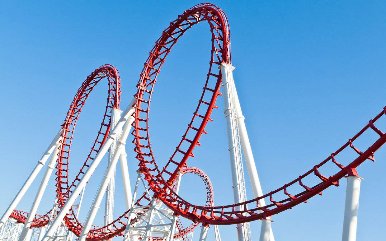 Roller Coaster 桌布 壁紙 — 一座高聳的紅色雲霄飛車，帶有白色支架，在晴朗的日子裡穿過清澈的藍天。