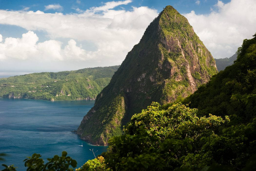 山景 桌布 壁紙 — 一座高聳的綠色山峰從深藍色的海洋中陡峭地升起，天空部分多雲。