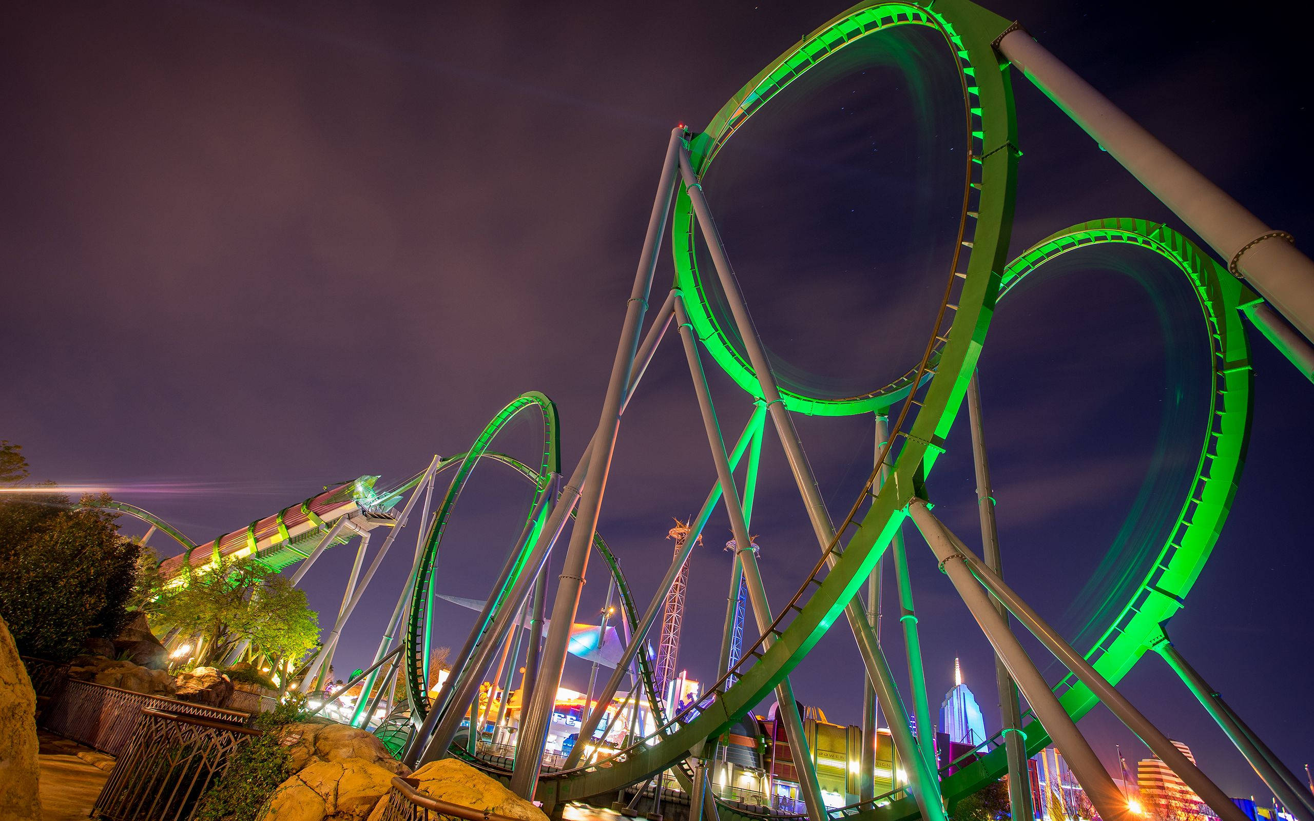 Roller Coaster 桌布 壁紙 — 一座高聳的綠色雲霄飛車在漆黑的夜空中閃耀，下方城市燈光閃爍。