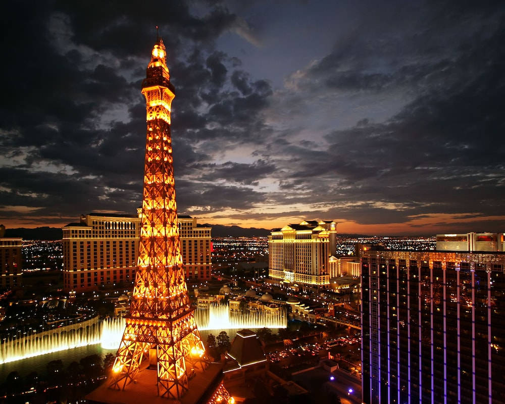 Eiffel Tower 桌布 壁紙 — 一座高聳的艾菲爾鐵塔複製品在暮色天空中溫暖地發光，映襯著拉斯維加斯充滿活力的天際線，伴隨著噴泉和霓虹燈。